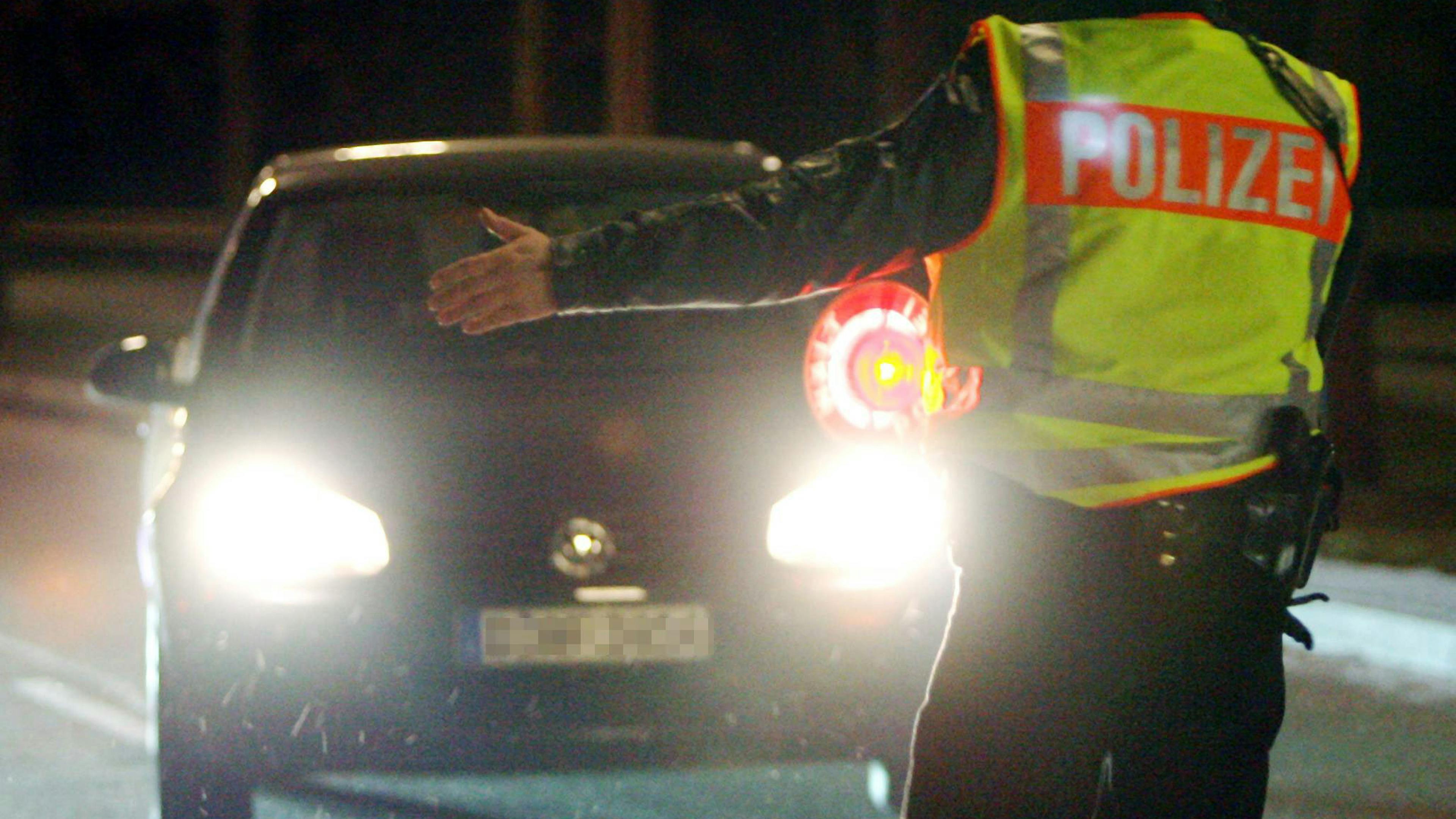 A policeman in a high-visibility vest signals a car with its high beams on to stop during a nighttime traffic check.