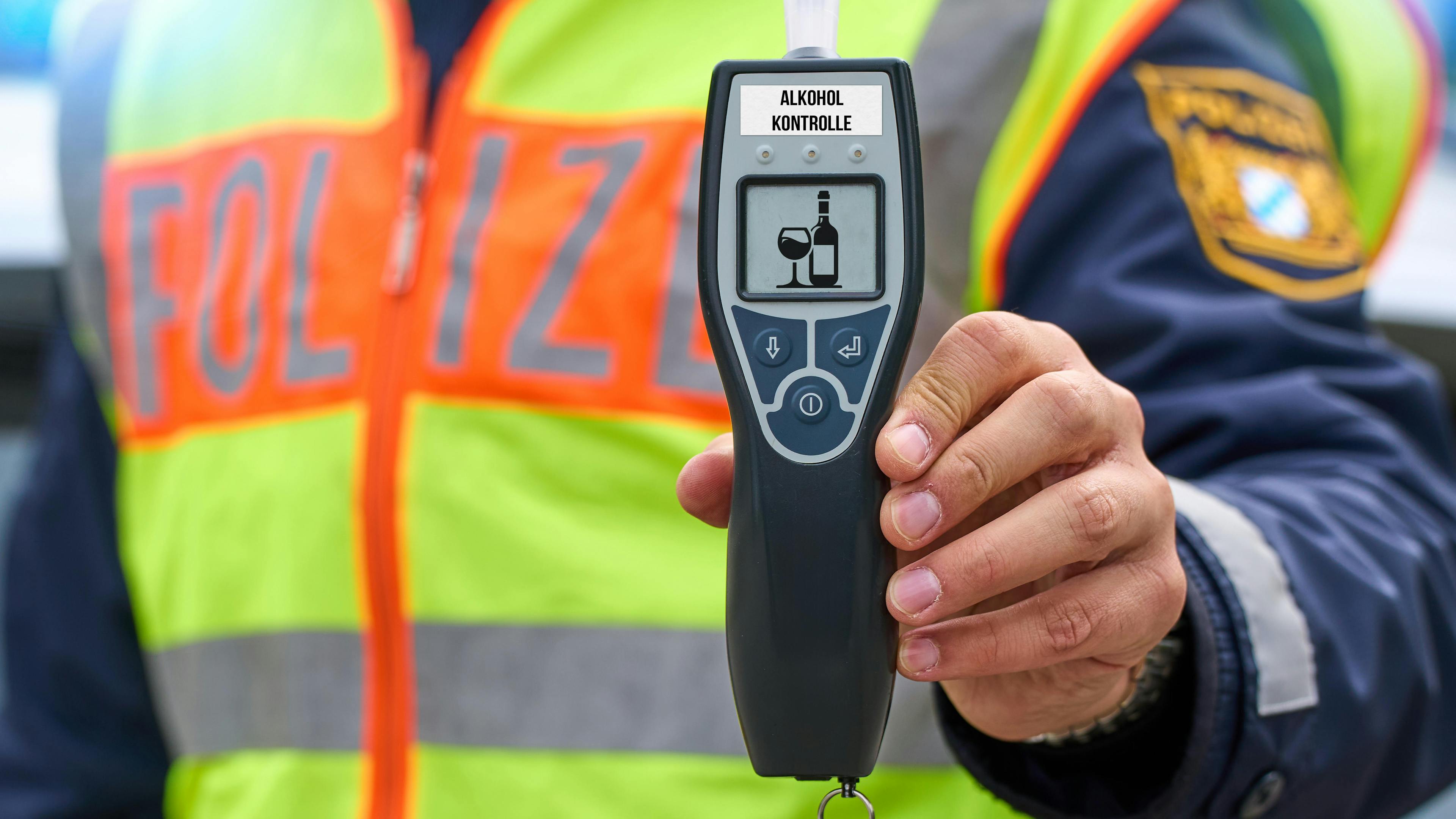 A police officer wearing a high-visibility vest holds a breathalyzer up to the camera during a traffic check.