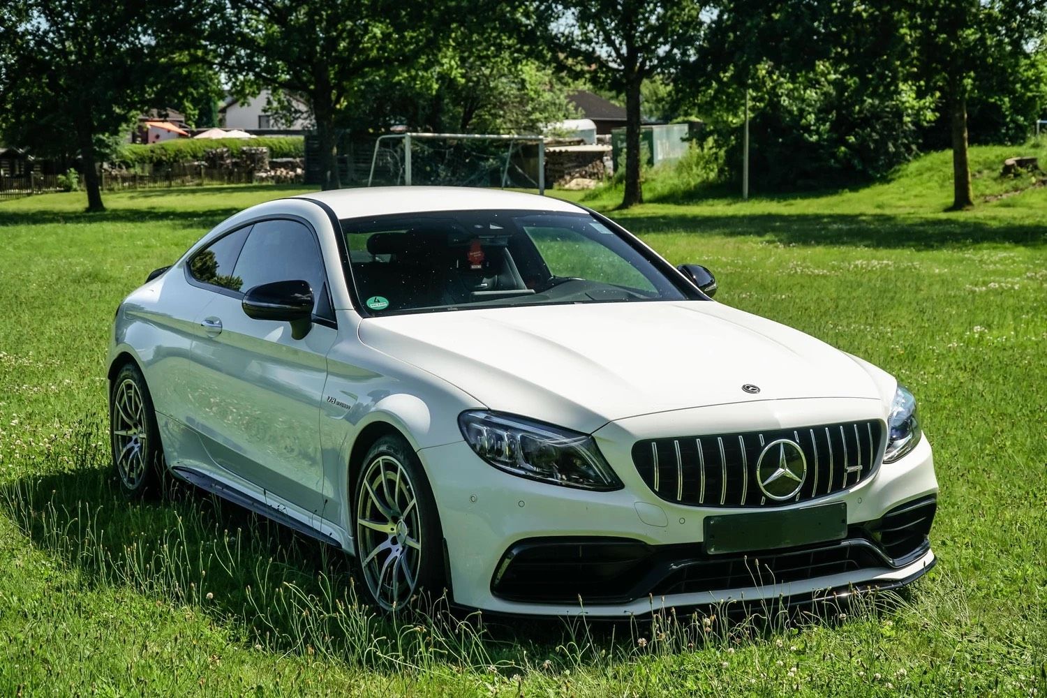 Ein weißes Mercedes-AMG C63 Coupé parkt auf einer Wiese.