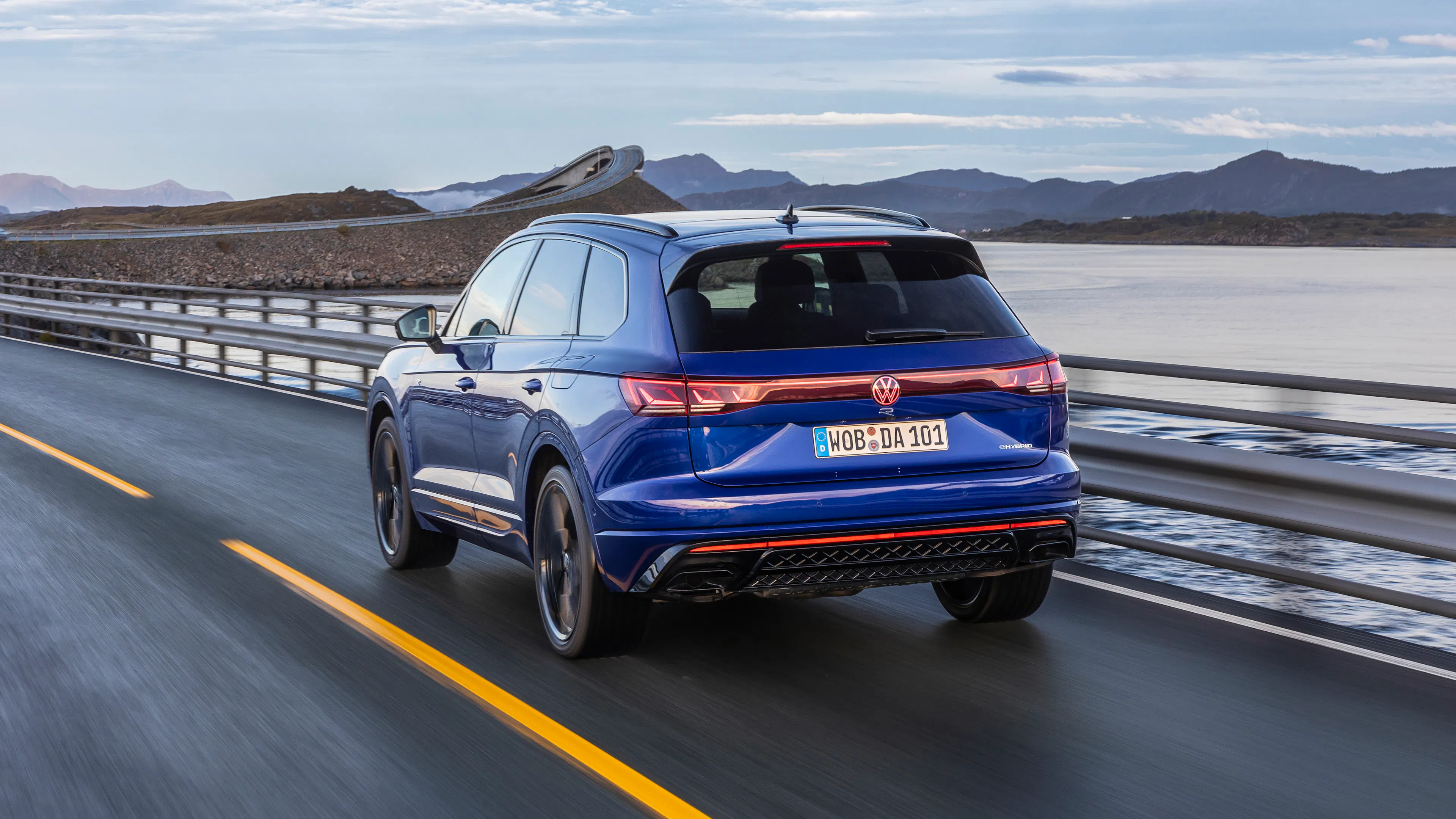 Ein blauer VW Touareg R fährt eine Küstenstraße entlang.
