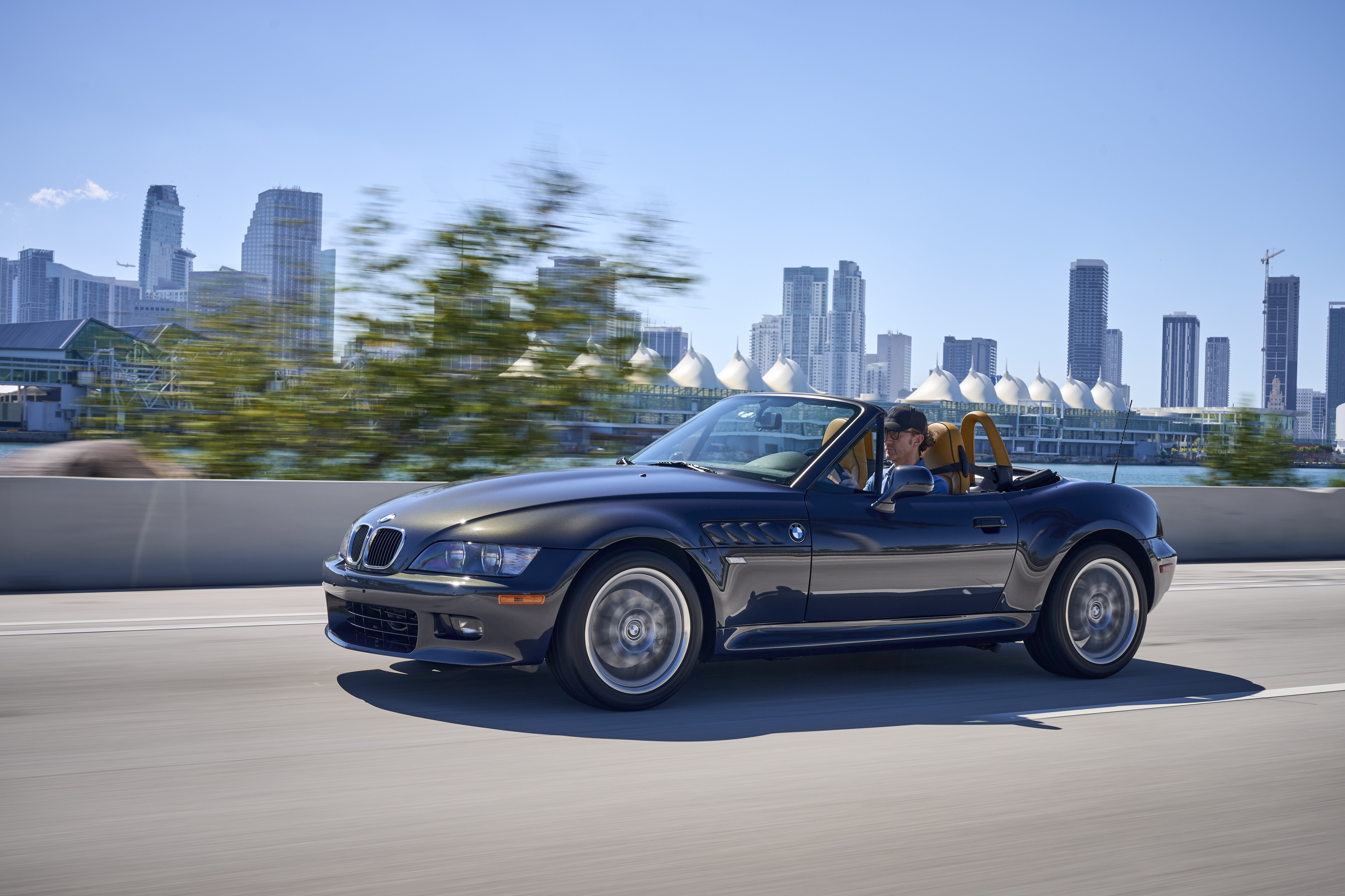 Ein offener BMW Z3 fährt vor einer Hochhaus-Skyline entlang.