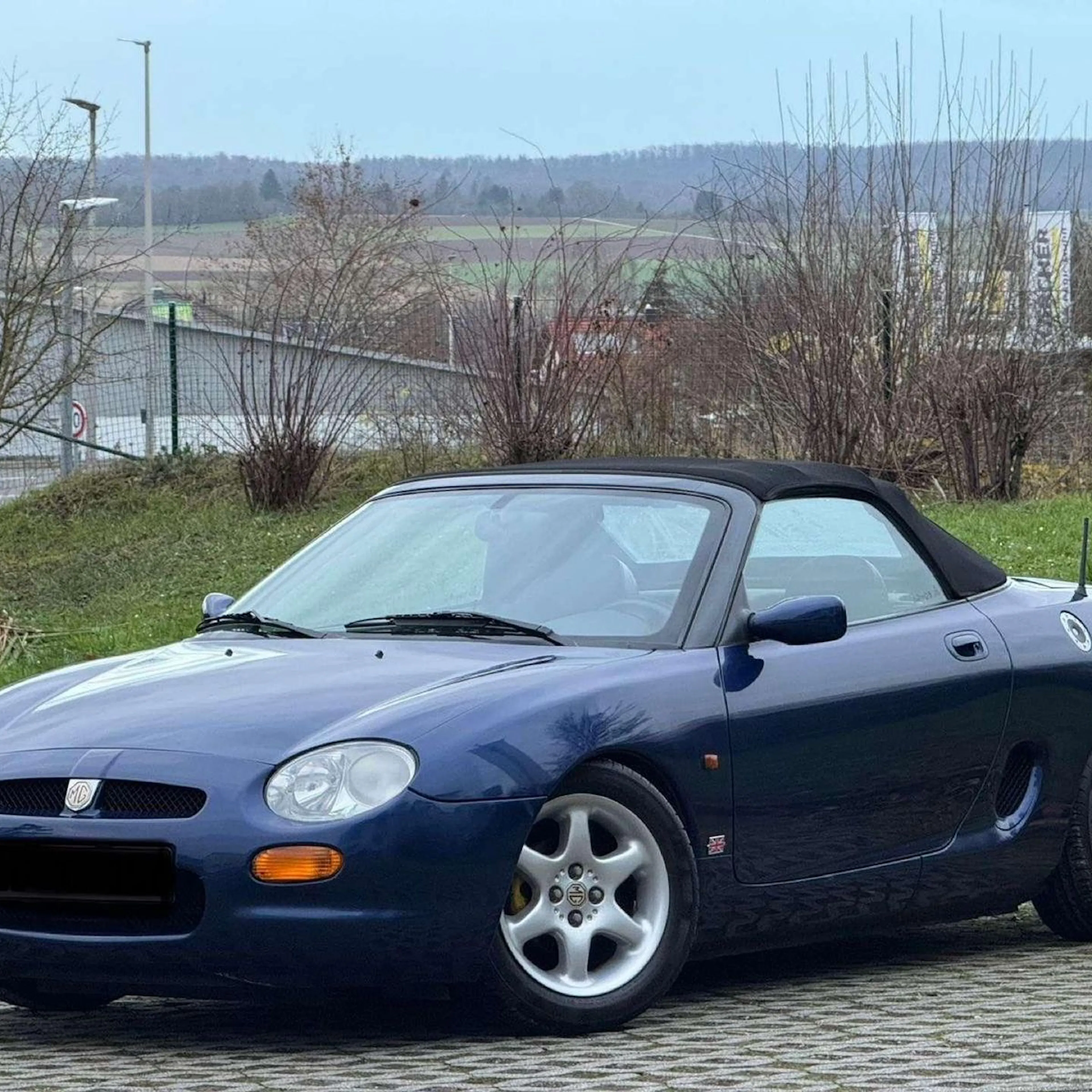 Ein blauer MG F steht auf einem Parkplatz.