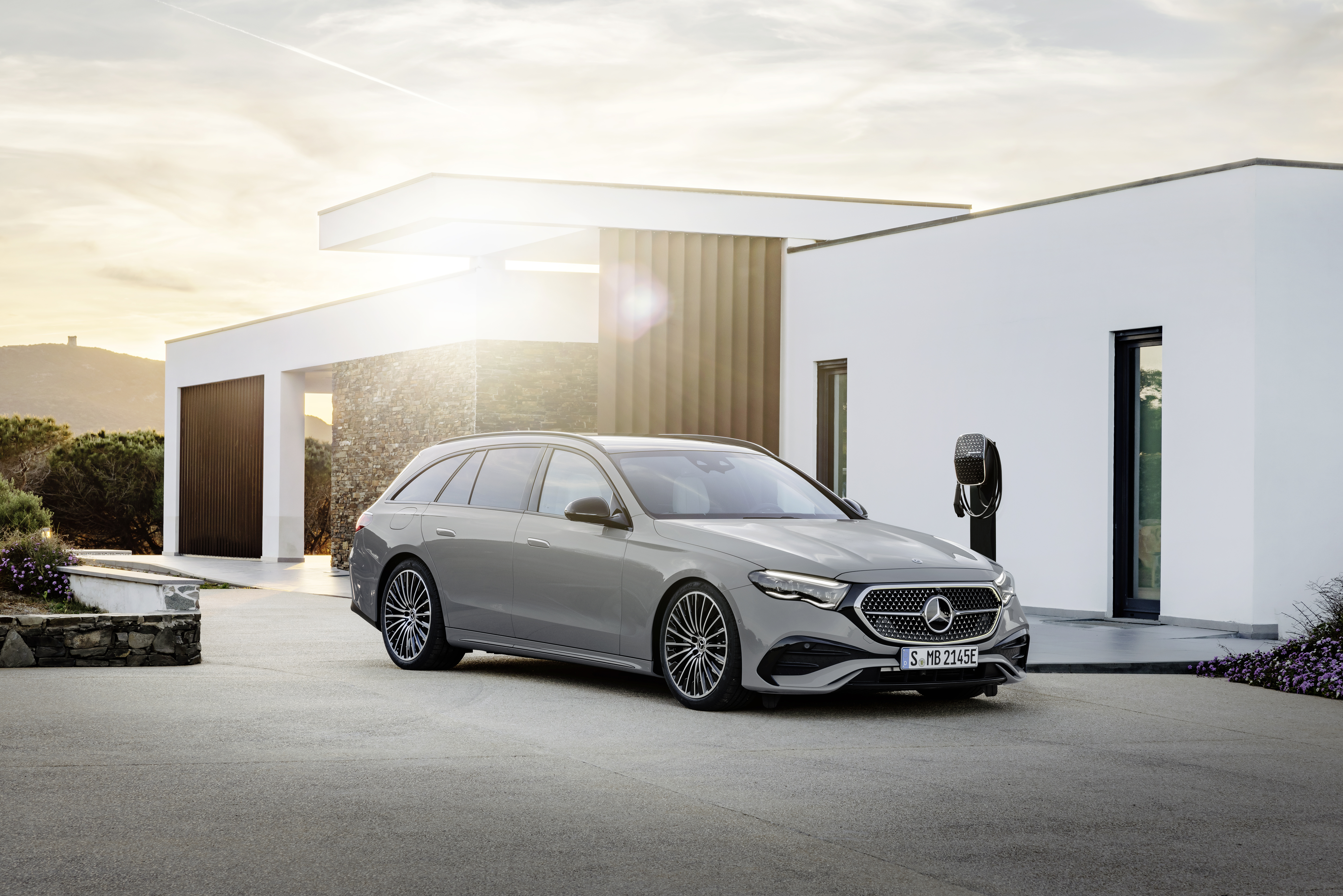 Ein grauer Mercedes E-Klasse Kombi parkt vor einem modernen weißen Neubau.