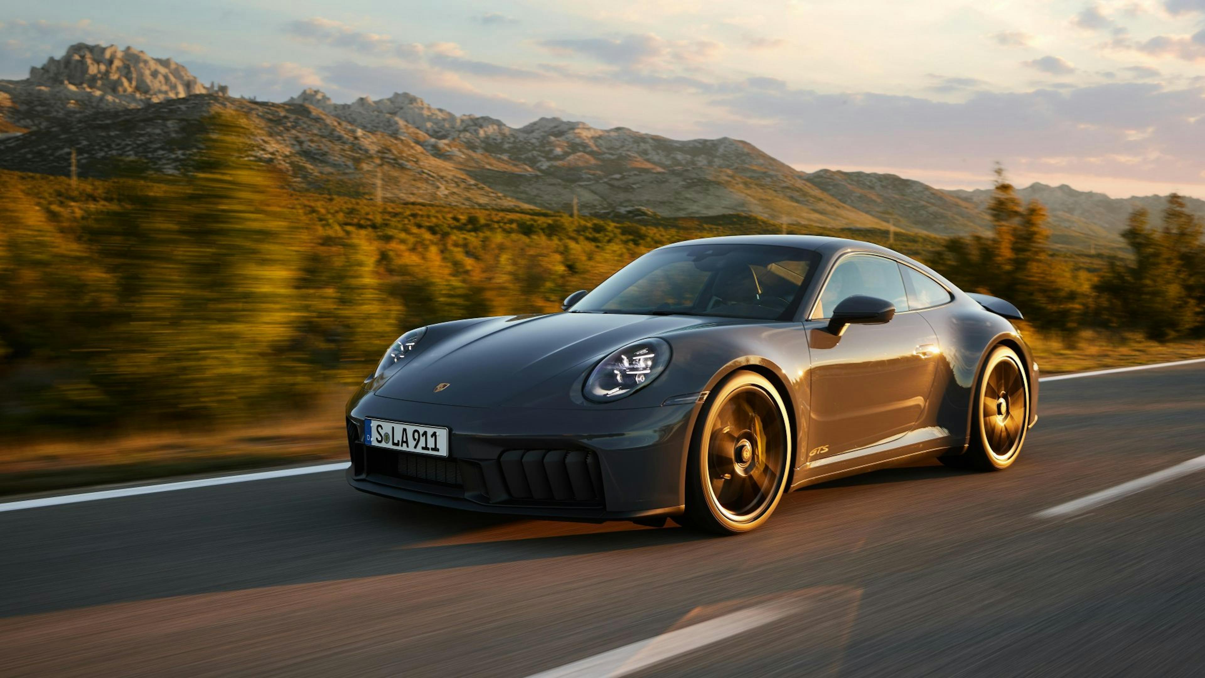 Ein grauer Porsche 911 fährt auf einer Landstraße im Gebirge.