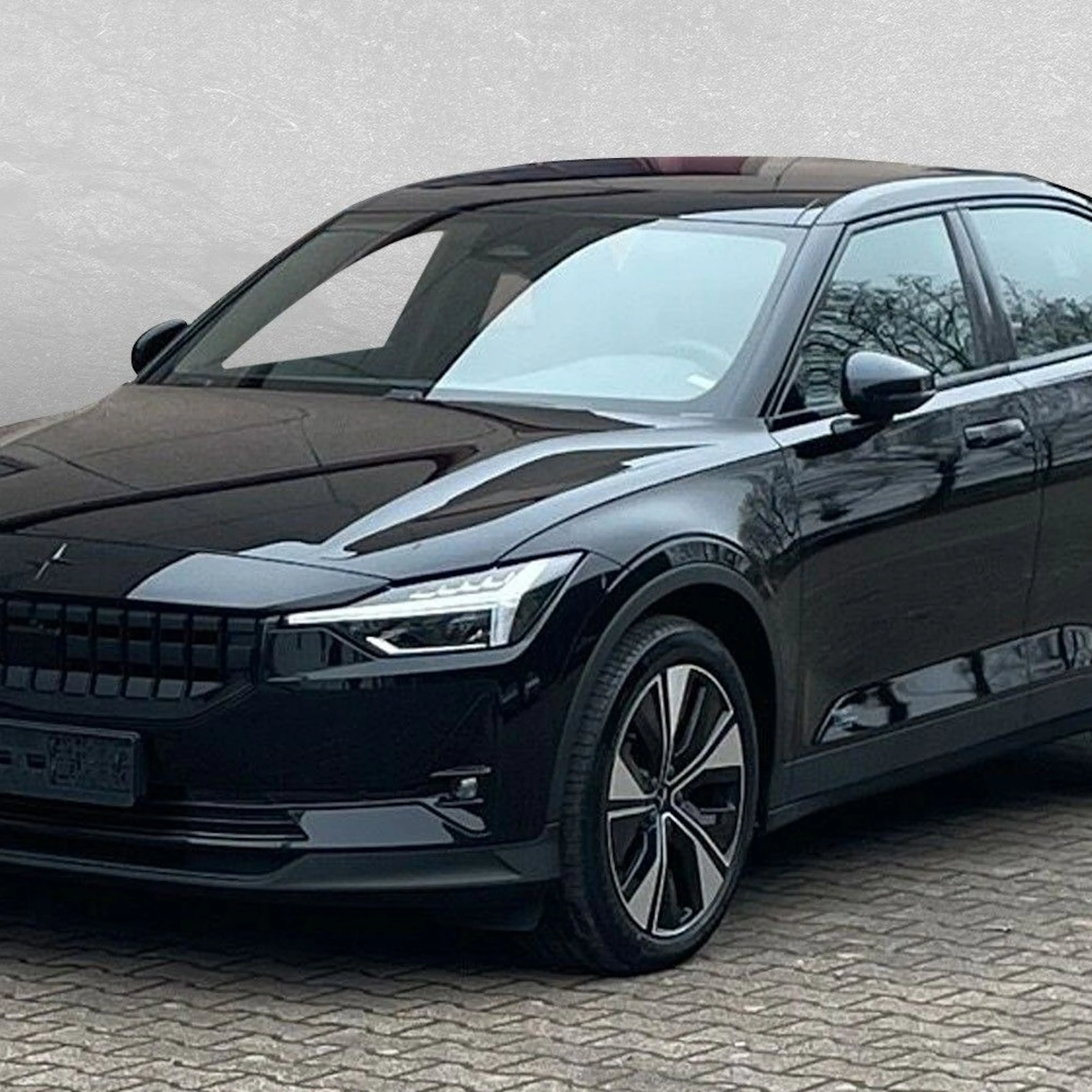 Schwarzer Polestar 2, geparkt auf Pflastersteinen vor grauer Wand.