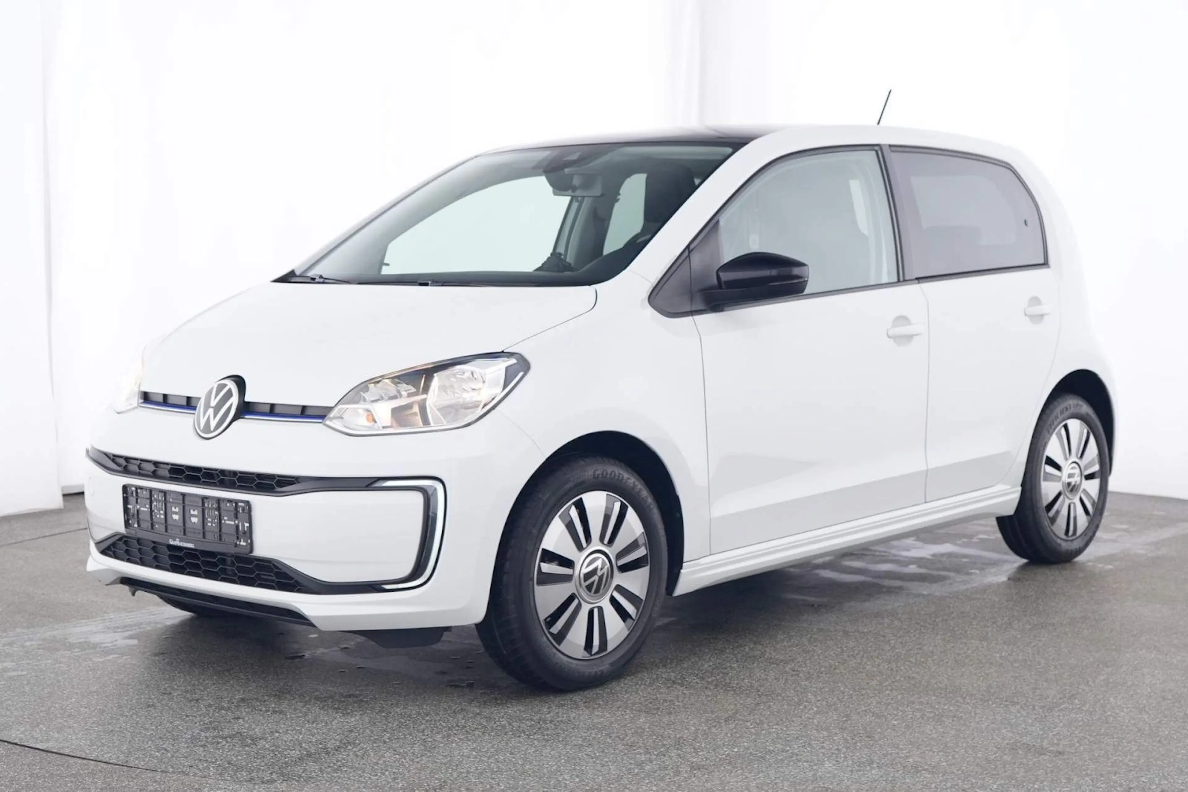 Weißer, moderner Kleinwagen von Volkswagen, seitlich abgebildet auf einem grauen Untergrund in einem hellen Raum.