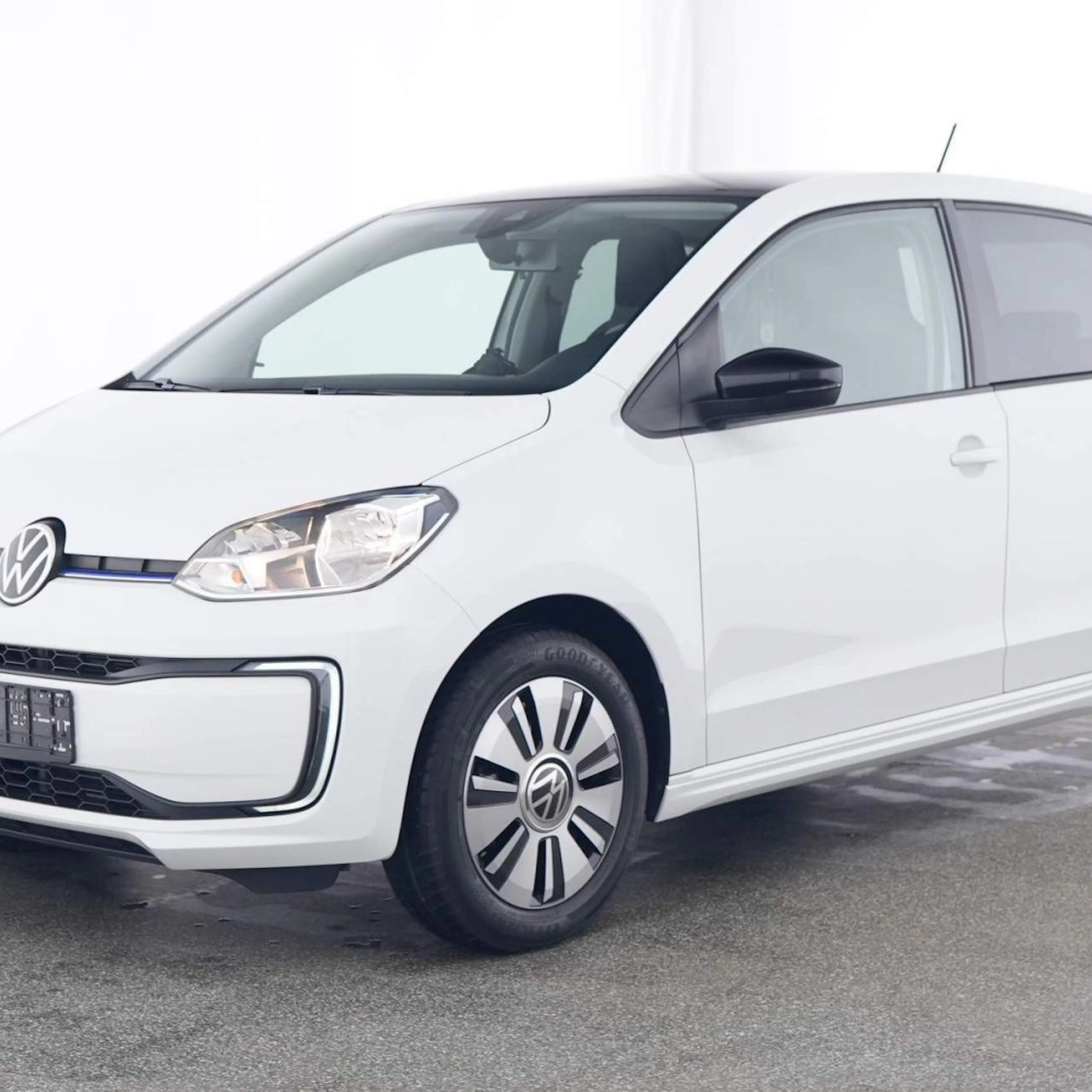 Weißer, moderner Kleinwagen von Volkswagen, seitlich abgebildet auf einem grauen Untergrund in einem hellen Raum.