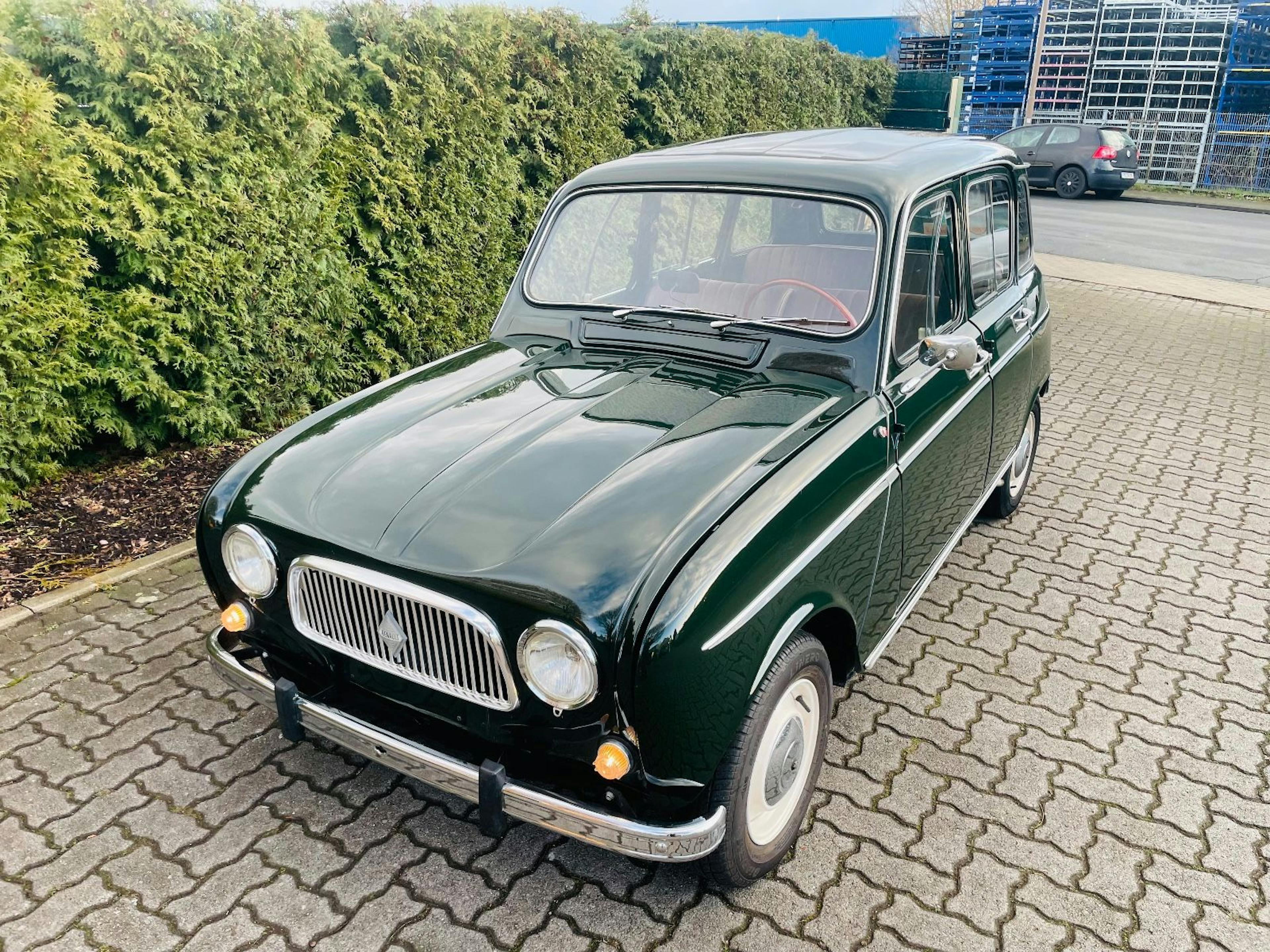 Ein grüner Renault 4 parkt vor einer Hecke.