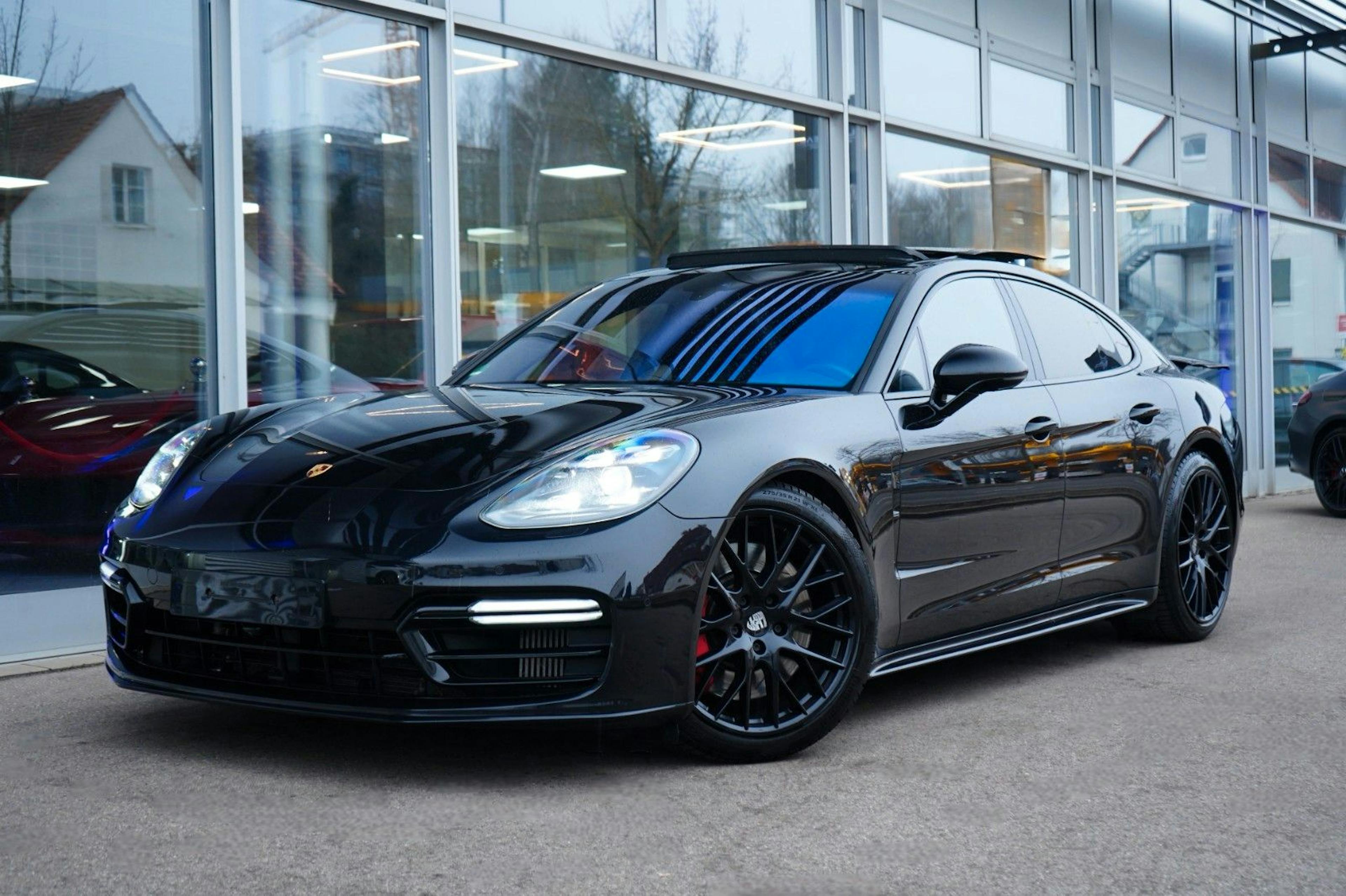 Ein schwarzer Porsche Panamera parkt vor einem Autohaus.