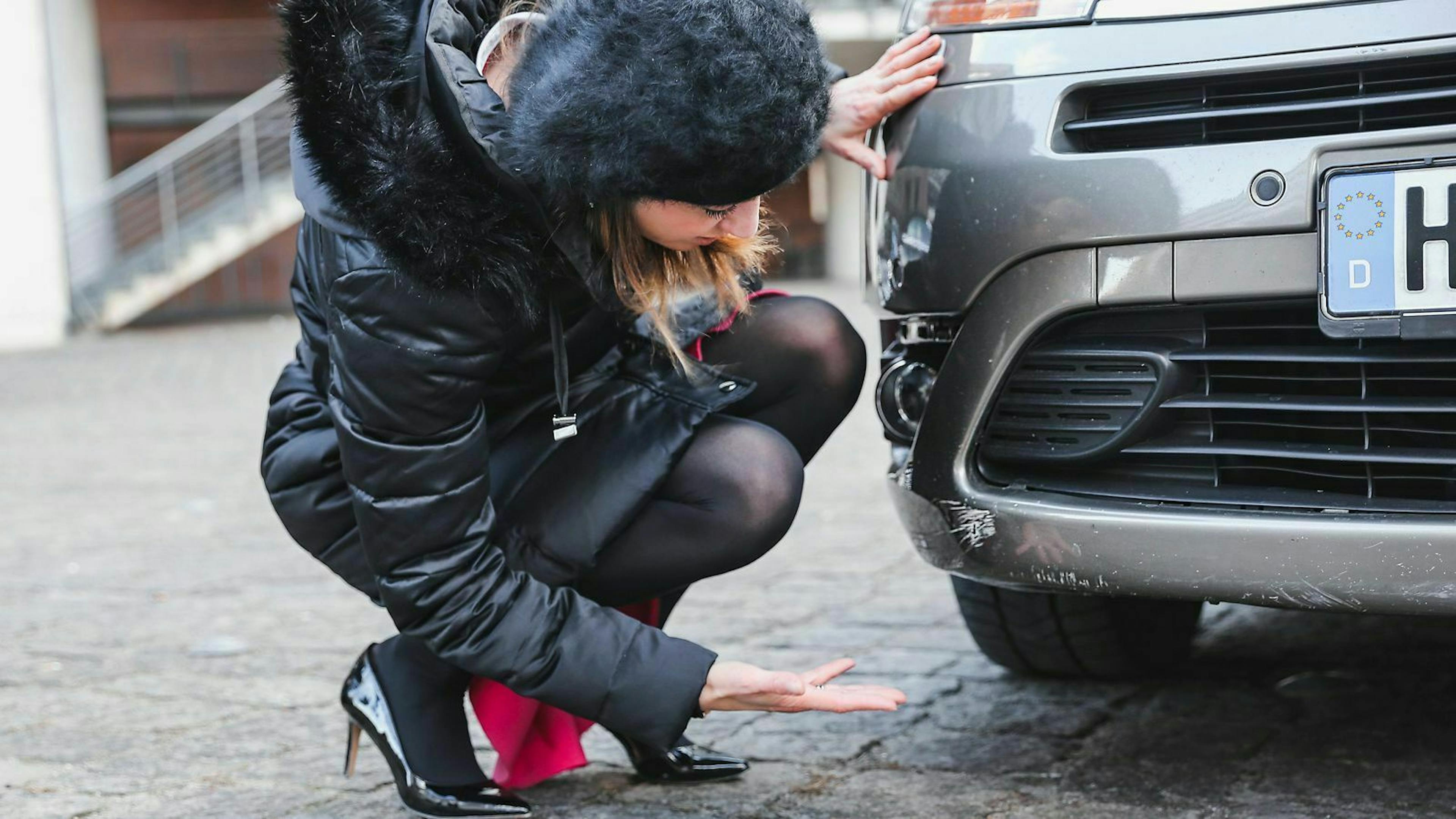 Eine Frau begutachtet einen Kratzer an ihrem Auto.
