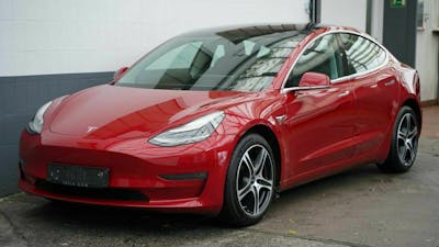 Ein roter Tesla 3 steht vor einem weiß-grauen Gebäude