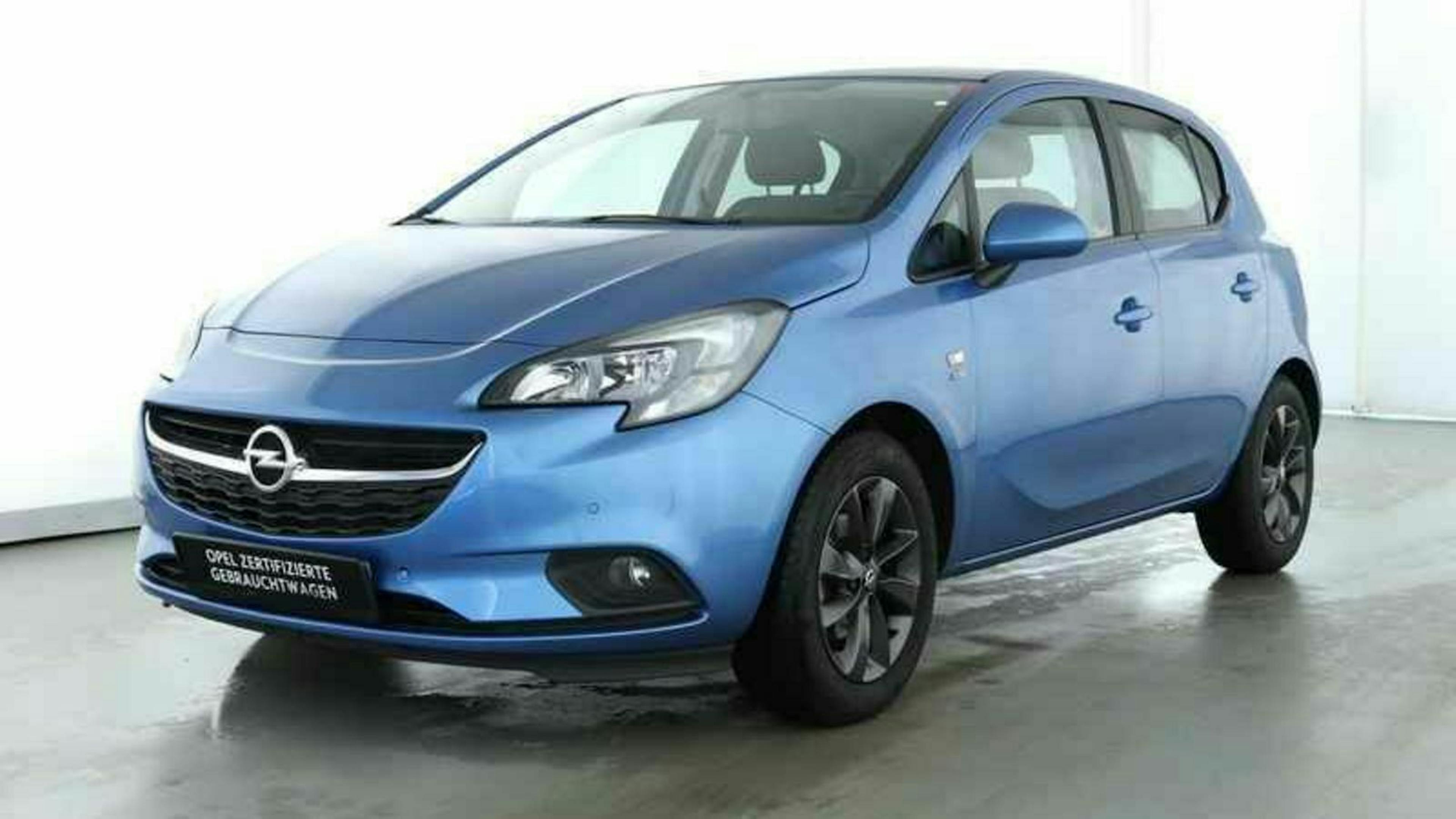 Blauer Opel Corsa Fünftürer steht in einem hellen Raum auf grauem Boden, leicht schräg von vorne fotografiert.
