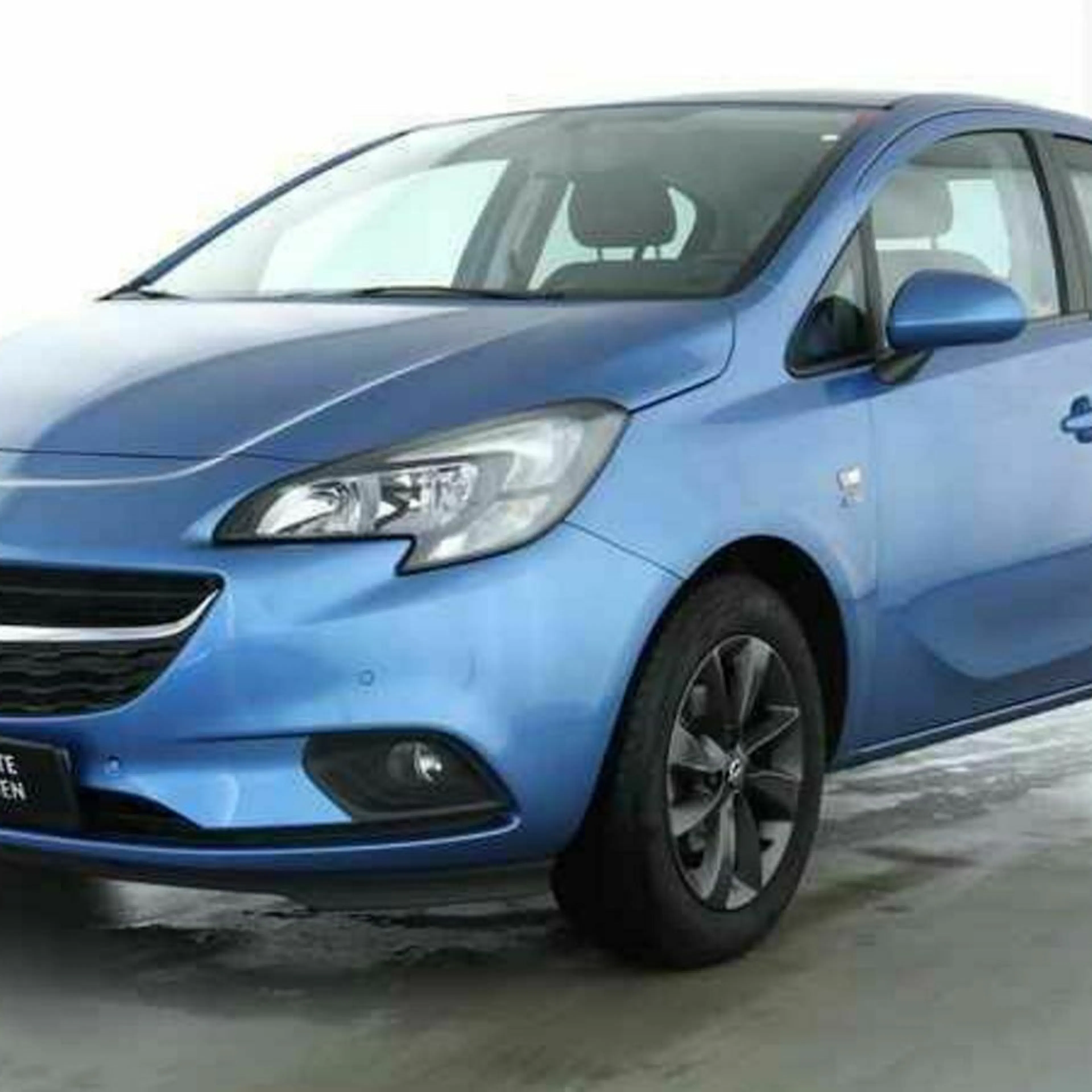 Blauer Opel Corsa Fünftürer steht in einem hellen Raum auf grauem Boden, leicht schräg von vorne fotografiert.