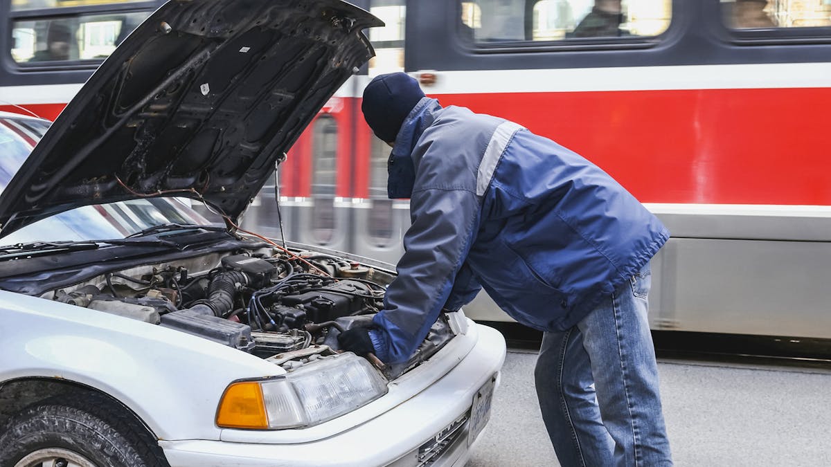 Jemand steht vor einem Auto mit geöffneter Motorhaube und inspiziert den Motorraum.
