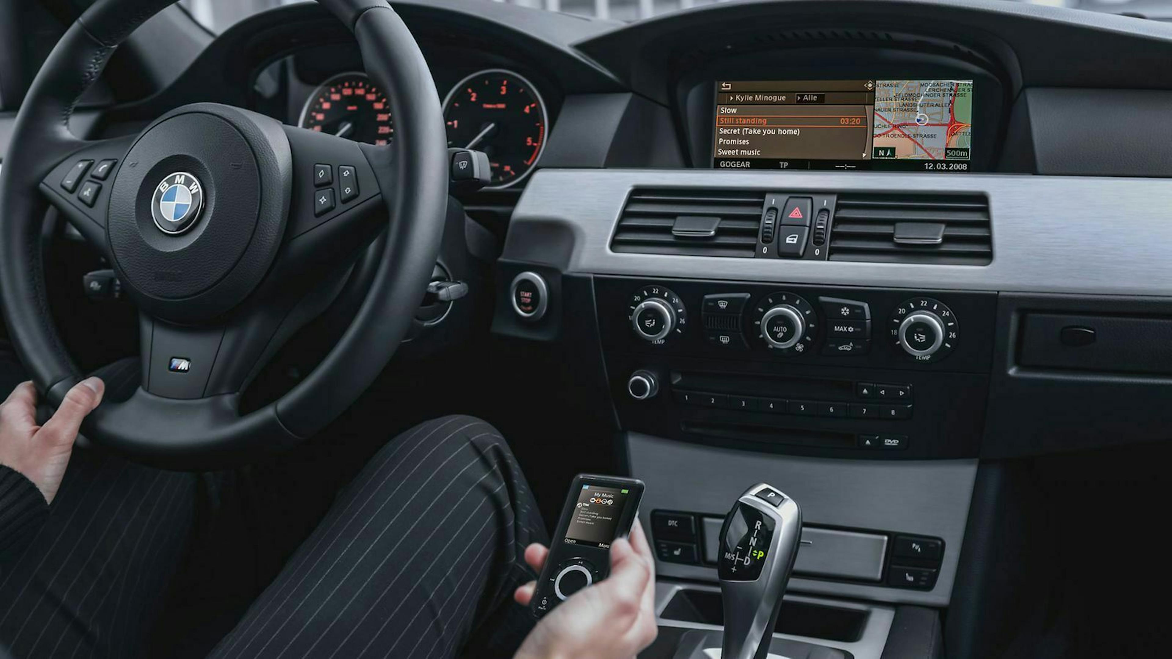 In einem BMW 5er der E60-Baureihe bedient der Fahrer einen mobilen Musikplayer.