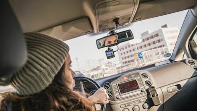 Eine junge Frau fährt in ihrem Auto durch die Stadt. In der Windschutzscheibe ist eine Dashcam montiert. 