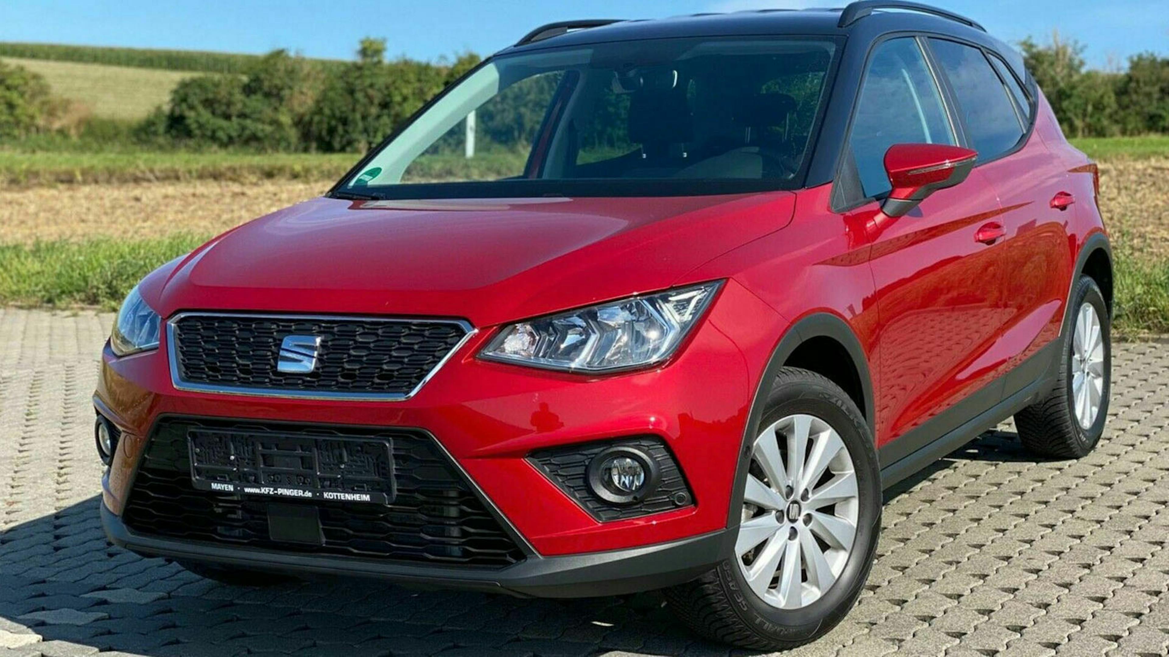 Ein roter Seat Arona steht auf einem Parkplatz vor einer Wiese