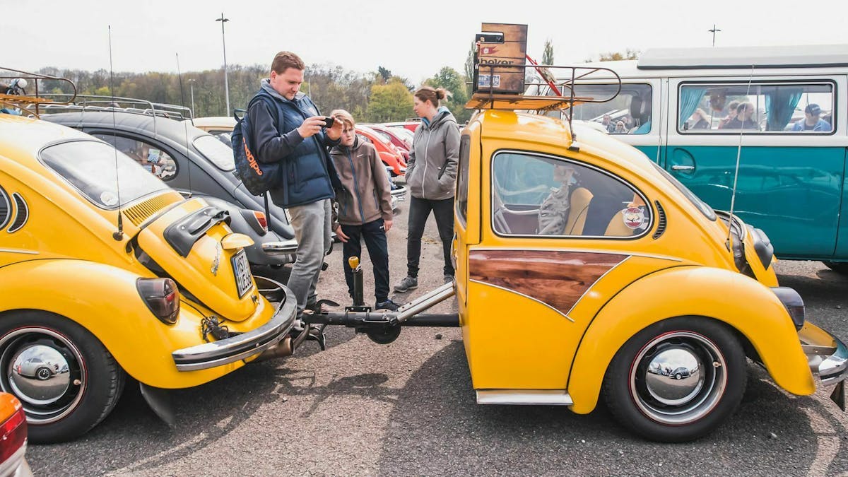Ein gelber VW Käfer parkt mitsamt Hänger - ebenfalls in Form eines Käfers - auf einem Autotreffen.