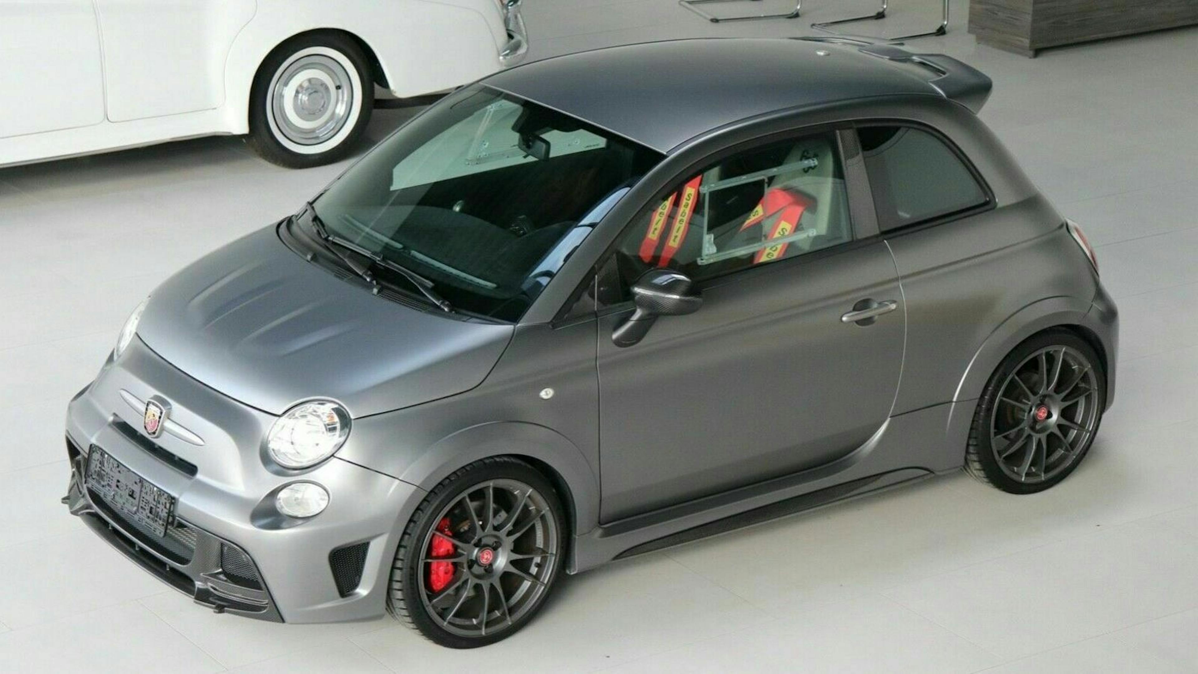 Grauer, sportlicher Kleinwagen mit schwarzen Felgen und roten Bremssätteln, in einer modernen Ausstellungshalle fotografiert.