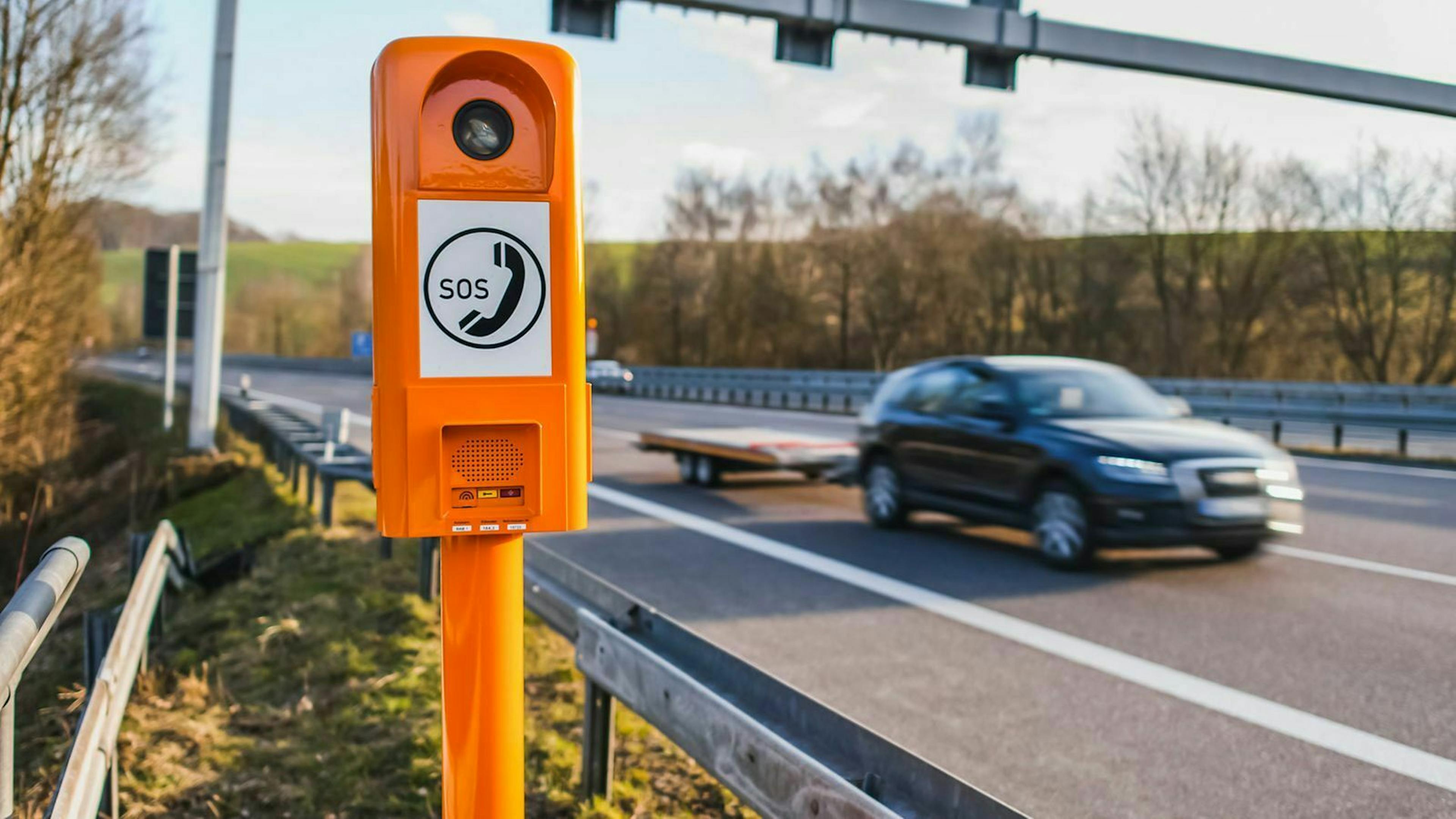 An einer Autobahn steht eine orangene Notrufsäule. 