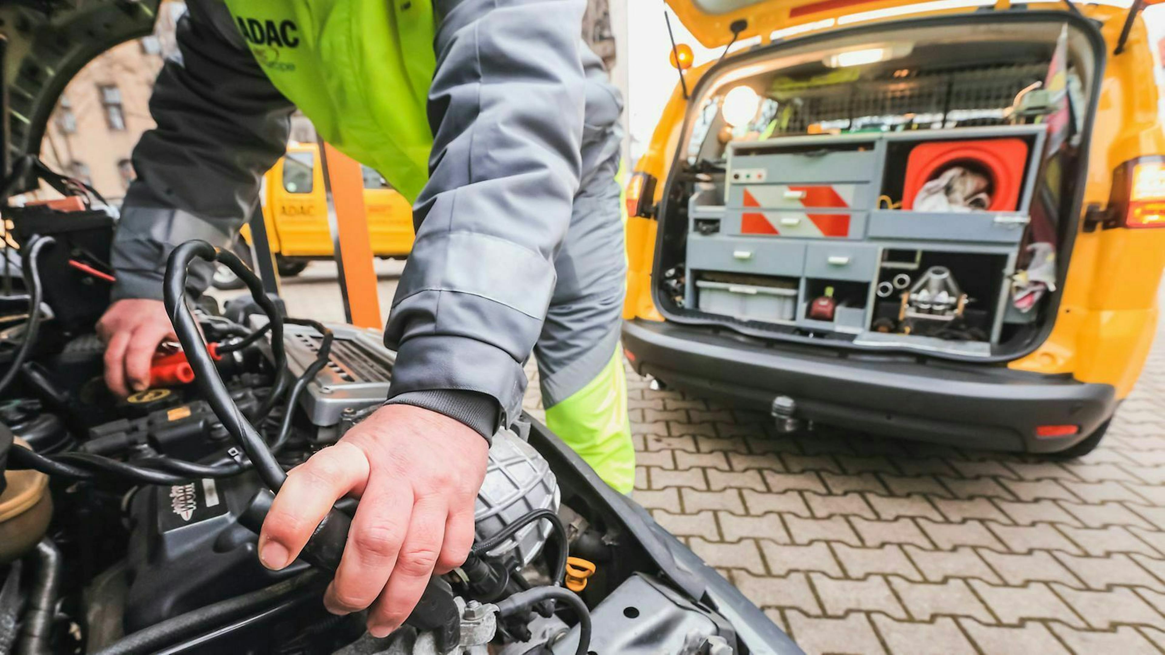 Ein ADAC-Mitarbeiter klemmt ein Starthilfekabel an eine Autobatterie an.