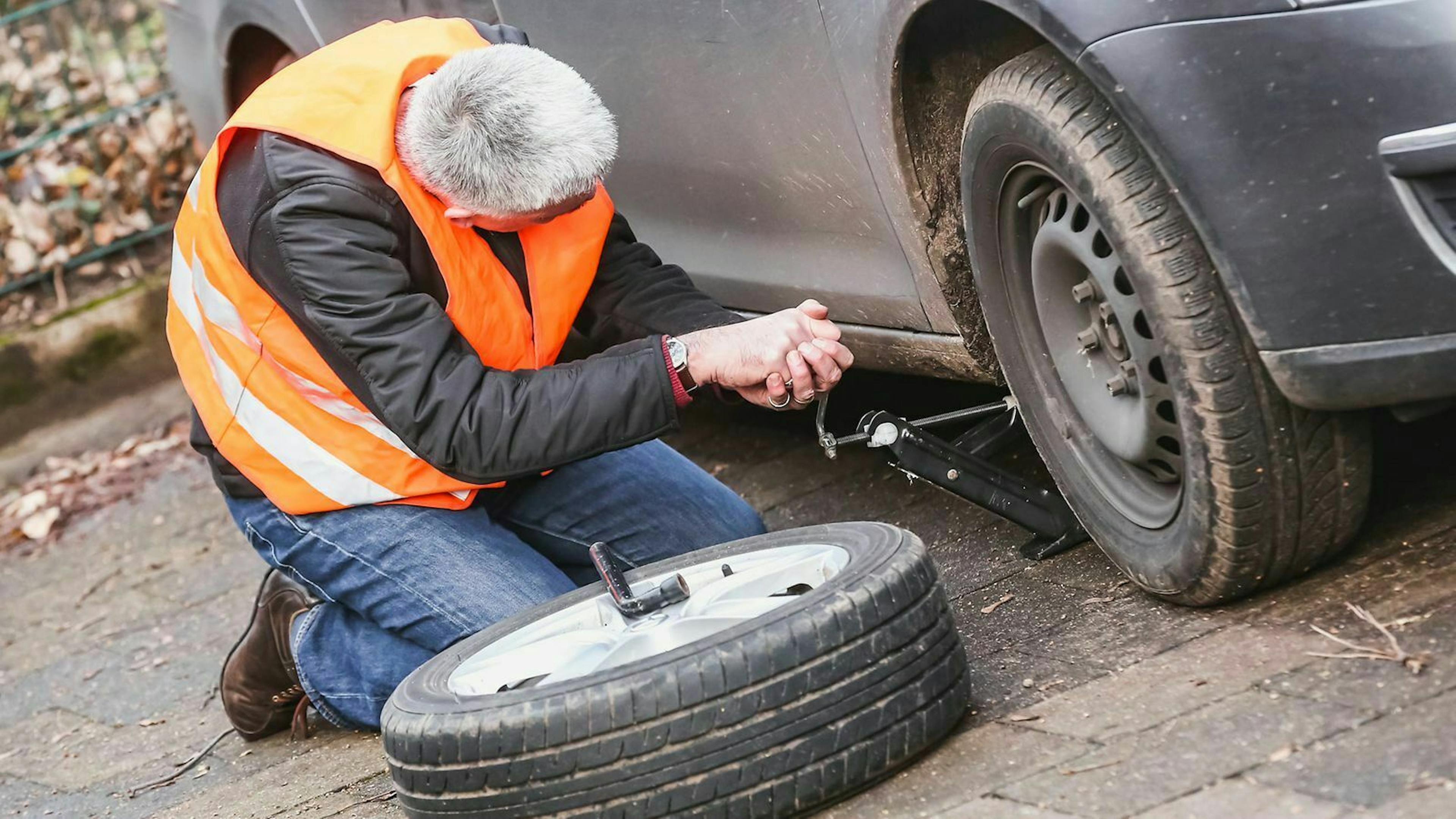 Ein Mann - in roter Warnweste gekleidet - wechselt eine Reifen an seinem Auto