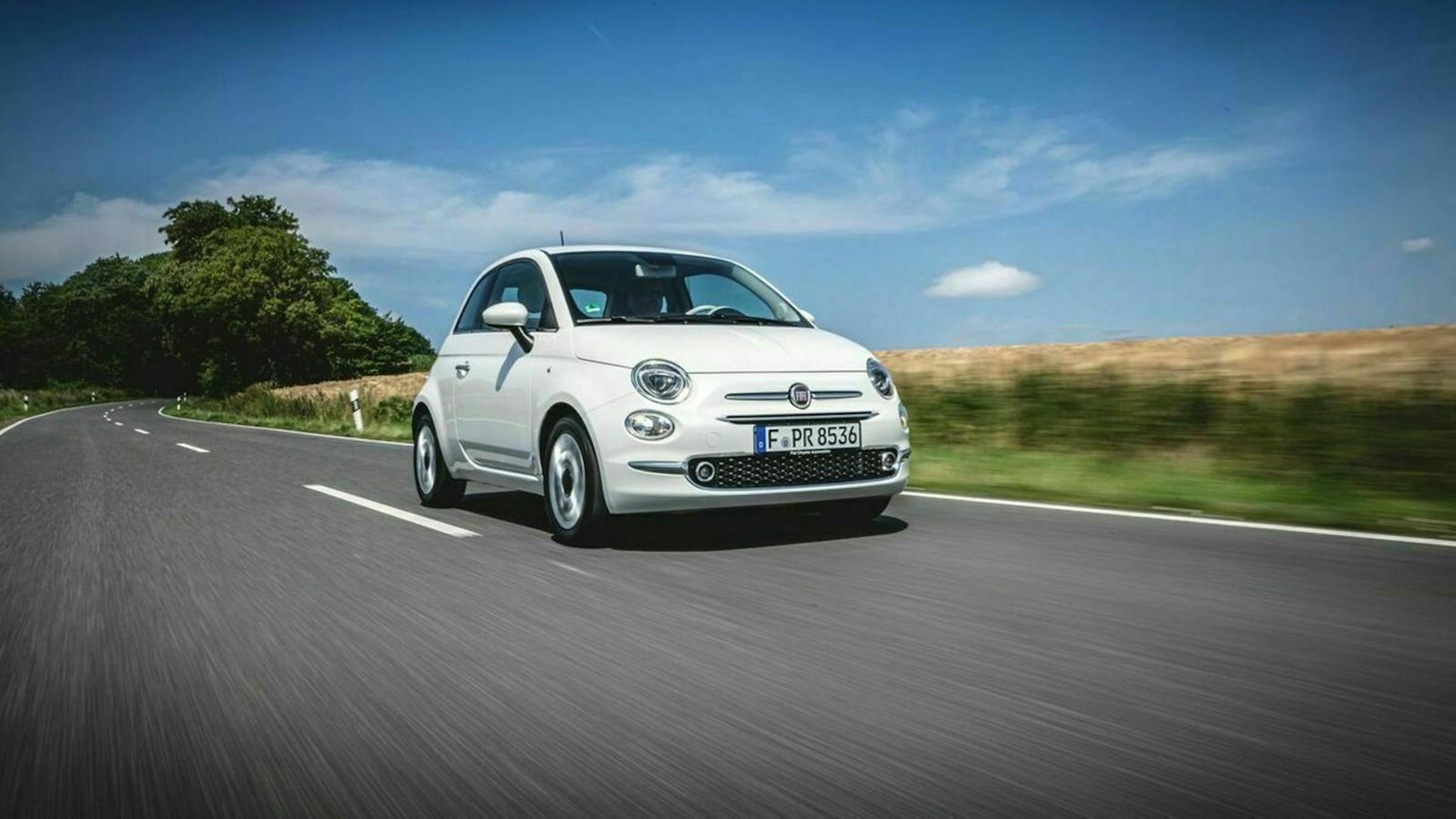 Ein weißer Fiat 500 fährt eine Landstraße entlang.