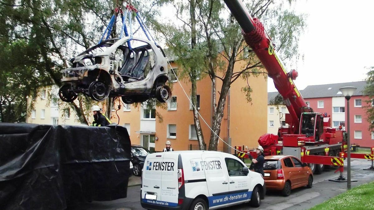 Ein ausgebranntes Elektroauto wird in einen Container verfrachtet
