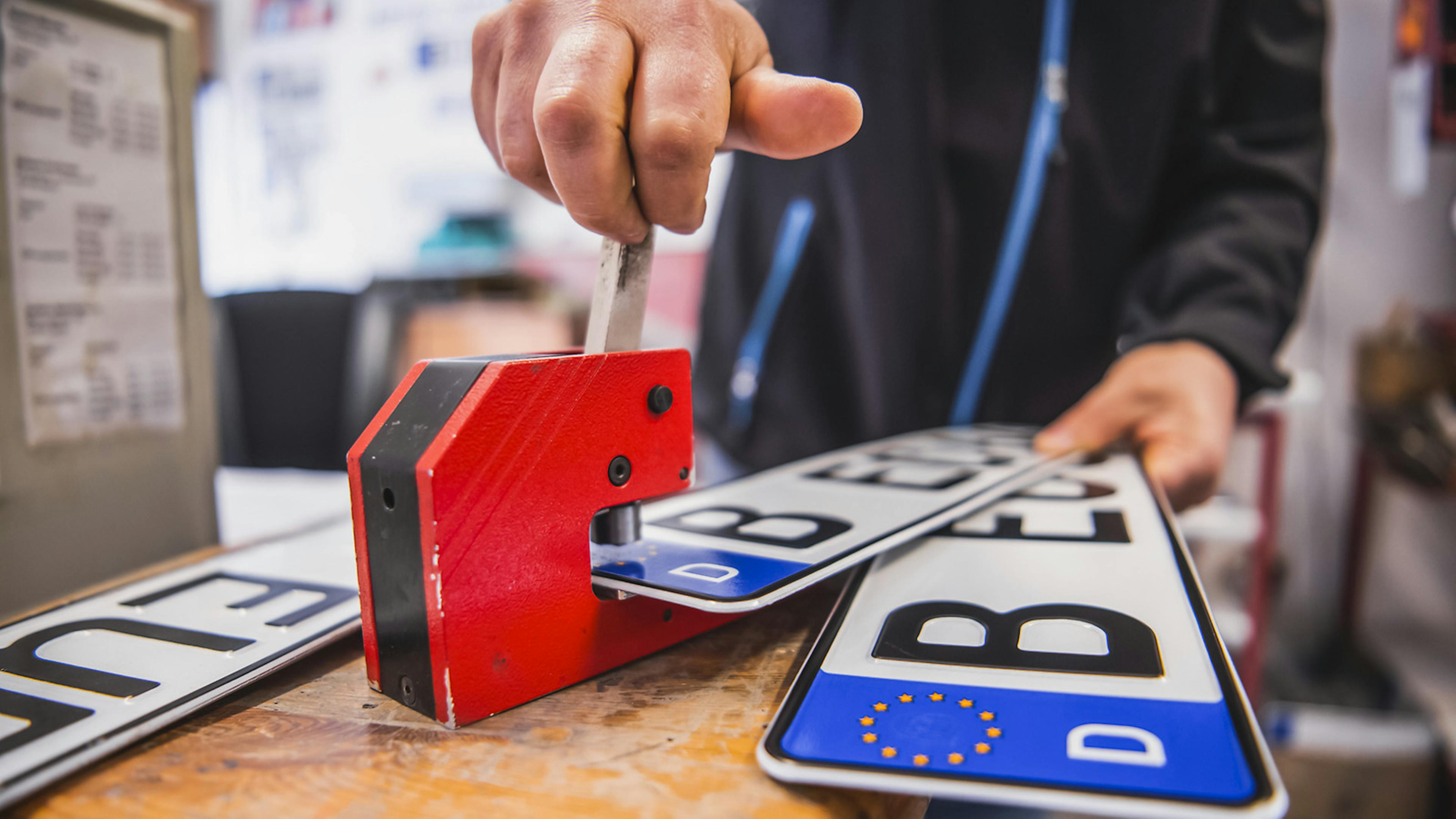 Jemand hält ein Nummernschild in eine Prägemaschine und betätigt den Mechanismus