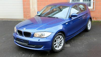 Ein blauer BMW 1er E87 steht vor einem Gebäude mit Backsteinwand