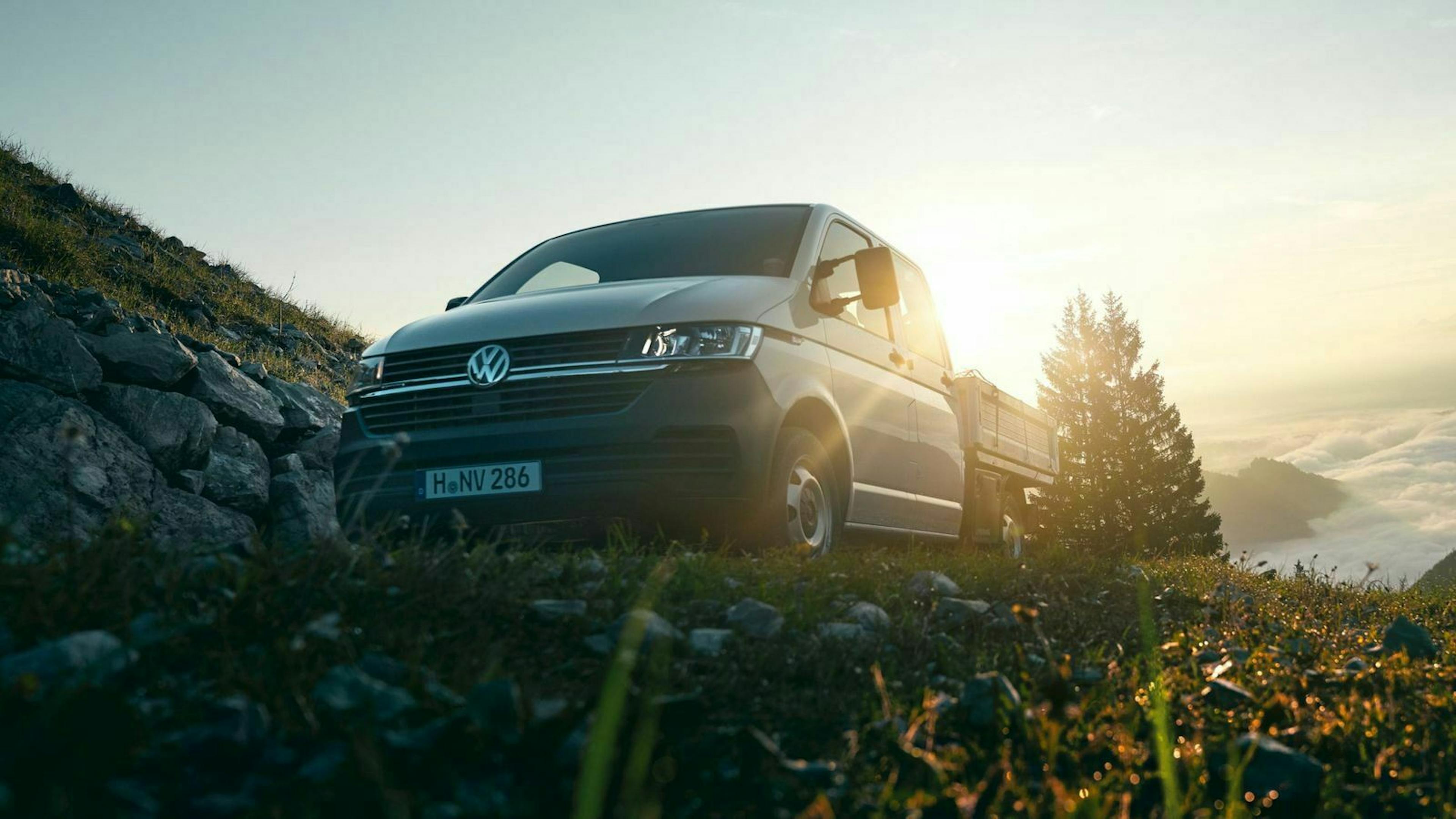 Ein grauer VW T6.1 Pritschenwagen fährt eine steile Bergstraße hinauf.