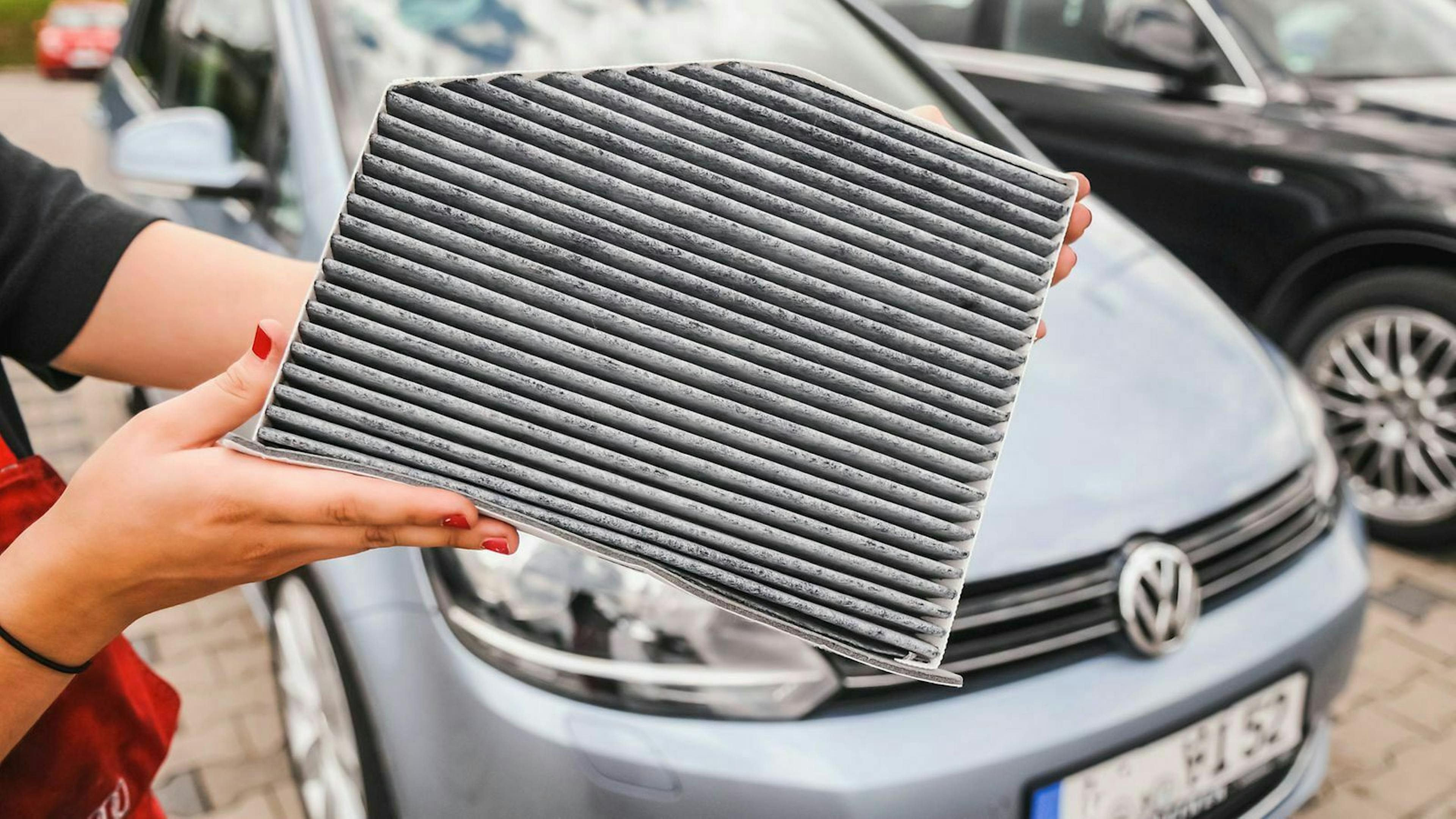 Eine Frau zeigt den Innenraumfilter eines VW Golf. 