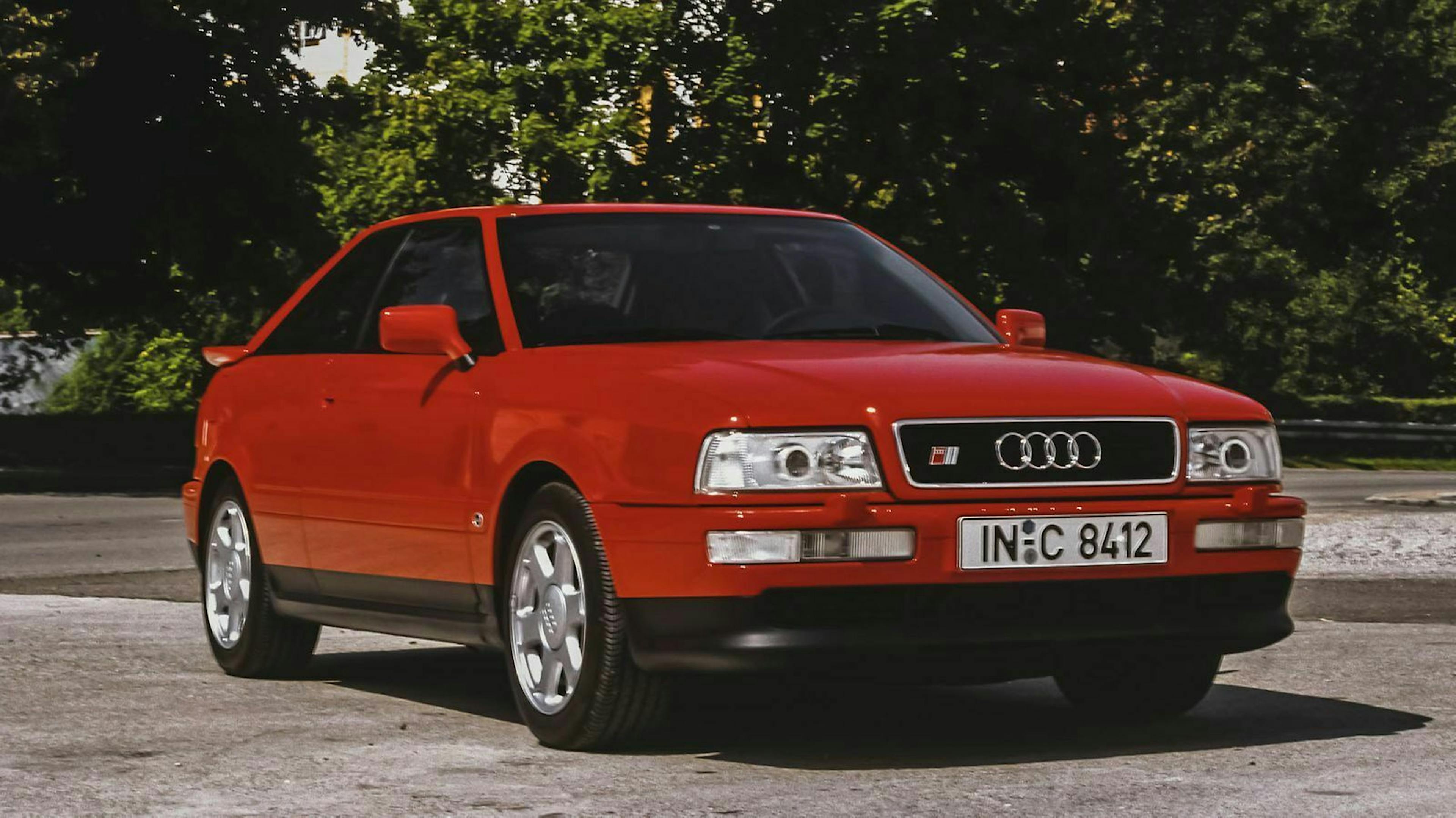 Ein roter Audi S2 steht vor grünen Bäumen.