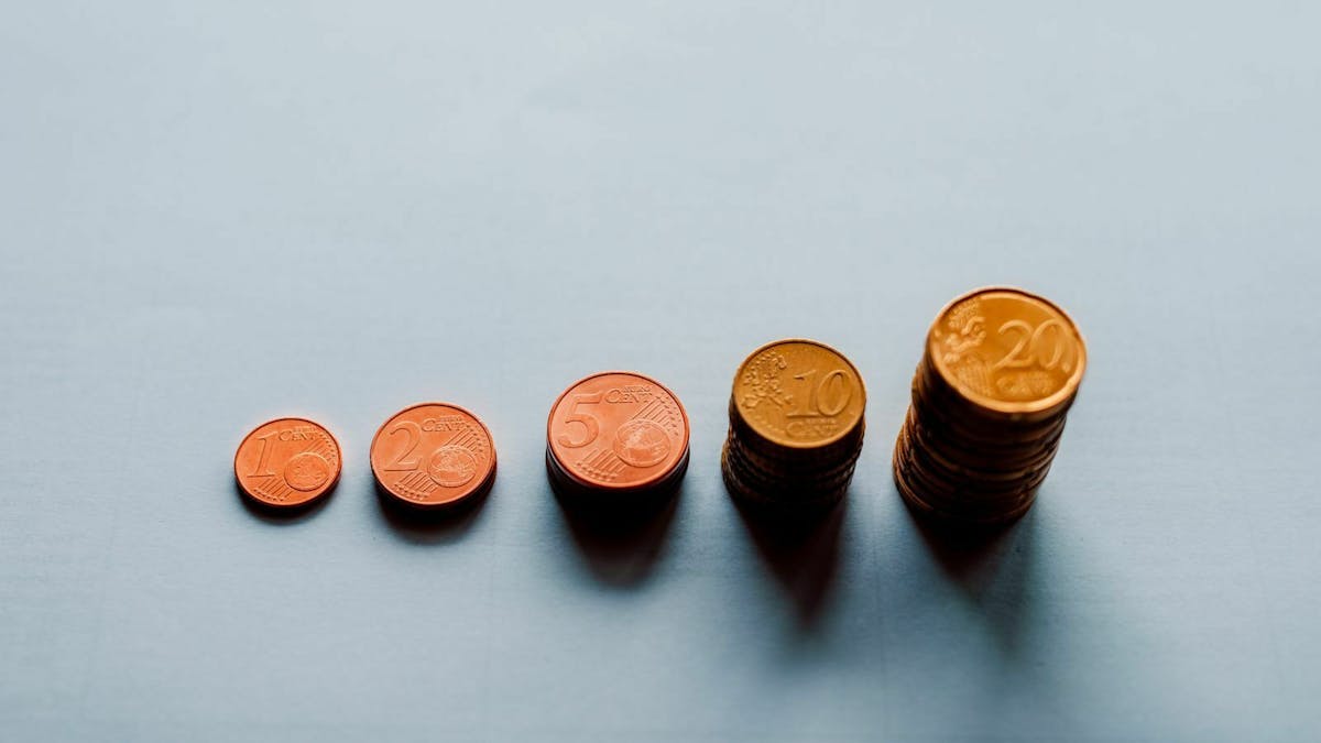 Fünf unterschiedlich hohe Stapel von Euro-Centmünzen befinden sich auf einem blau-grauen Untergrund