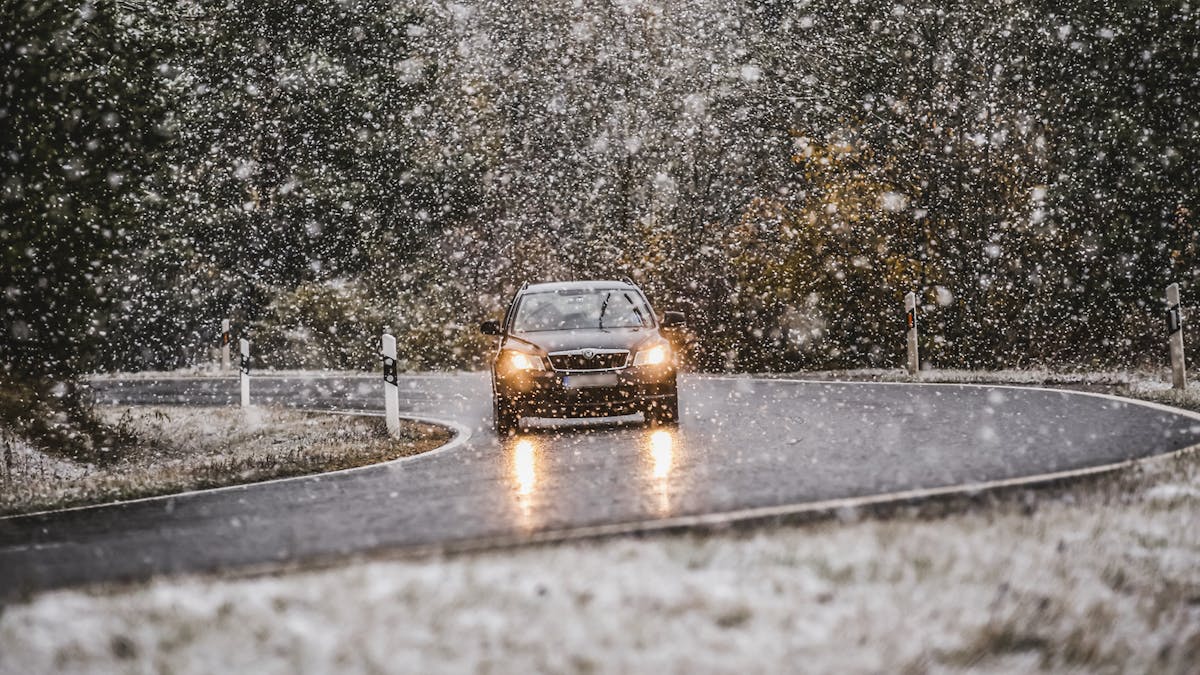 Ein Auto fährt auf einer Landstraße durch starken Schneefall.