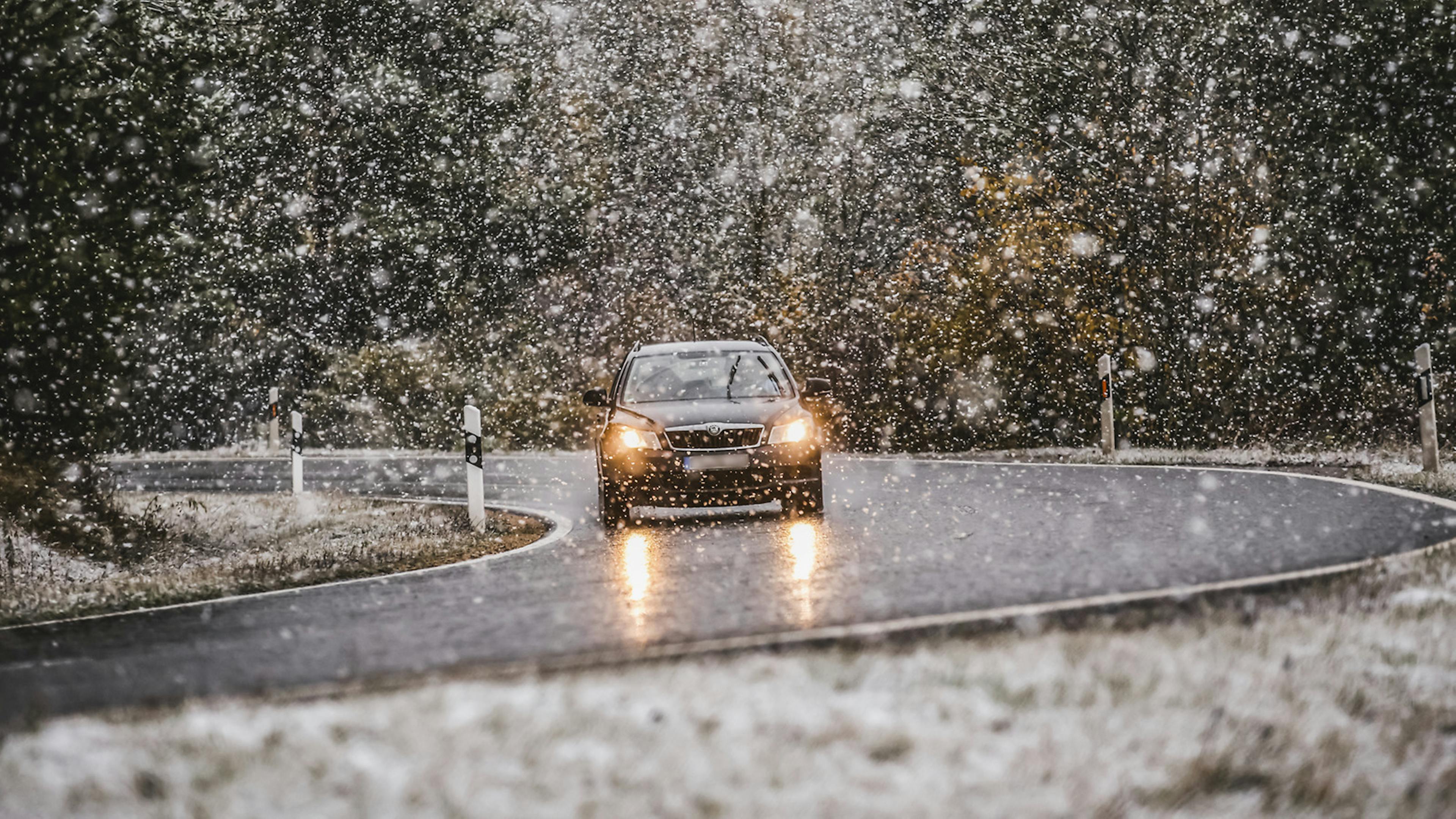 Ein Auto fährt auf einer Landstraße durch starken Schneefall.