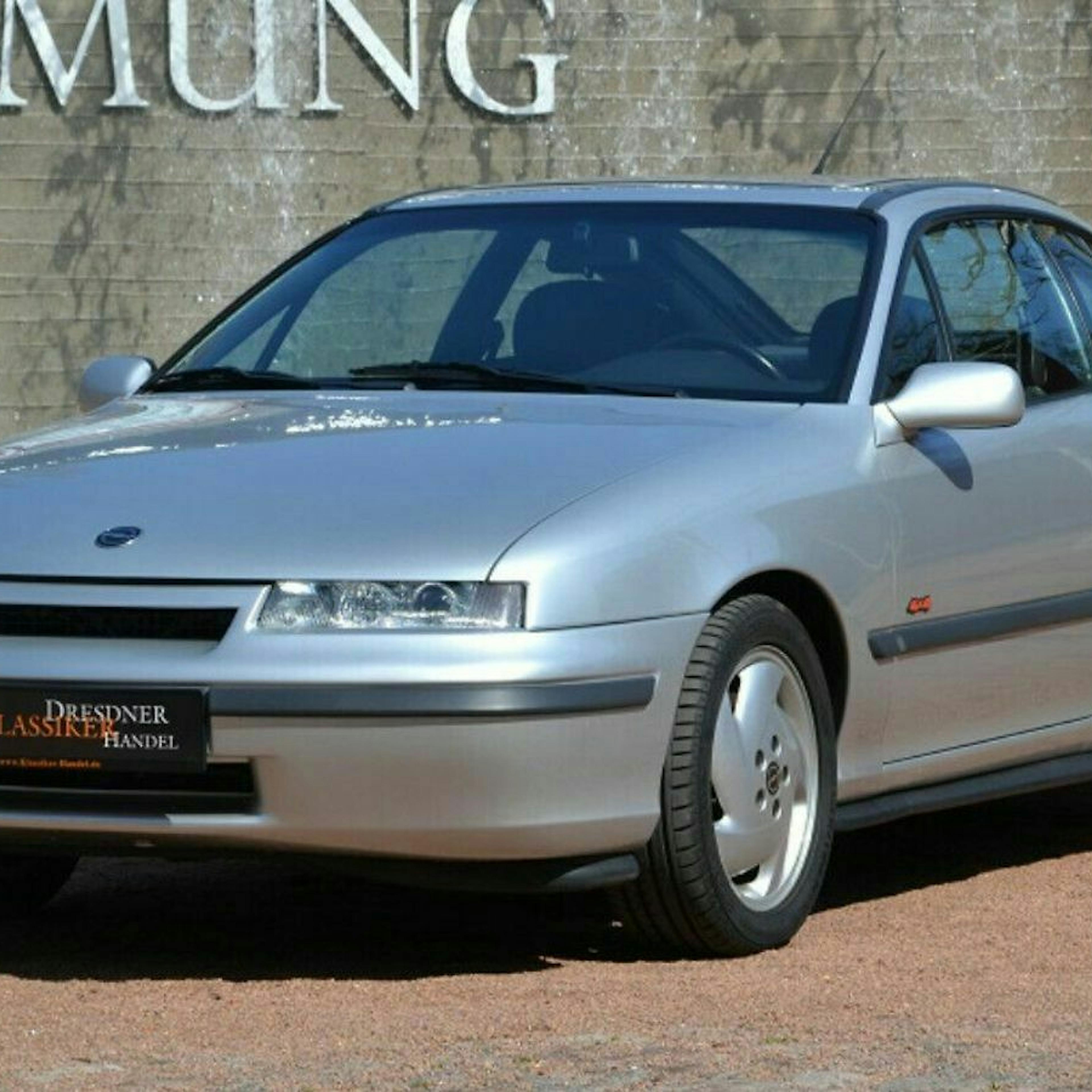 Ein silberner Opel Calibra Turbo Oldtimer steht vor einer grauen Wand.