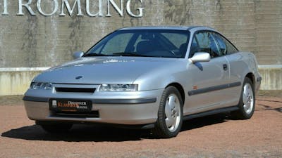 Ein silberner Opel Calibra Turbo Oldtimer steht vor einer grauen Wand.