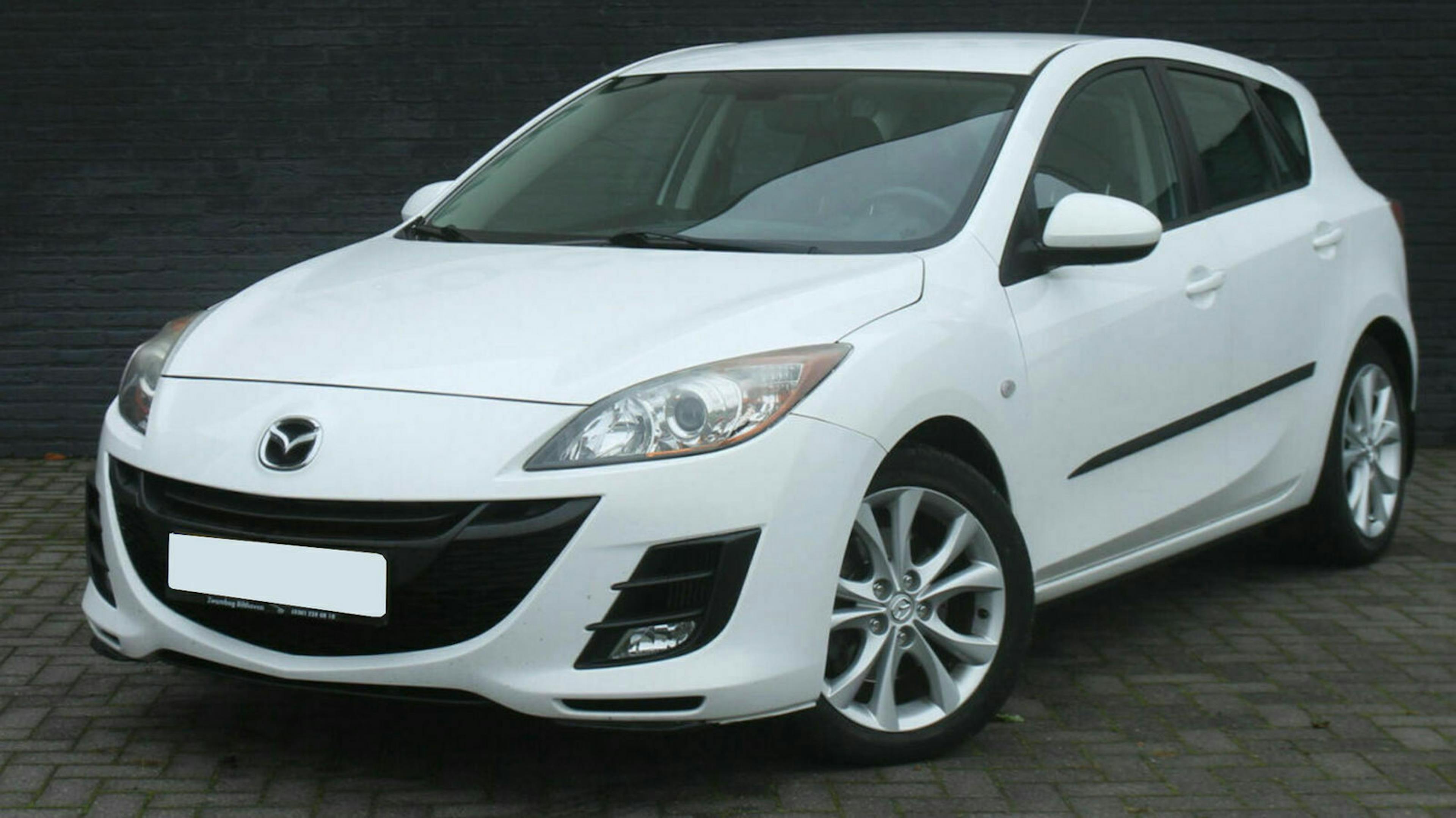 Ein weißer Mazda 3 BL steht vor einer grauen Wand