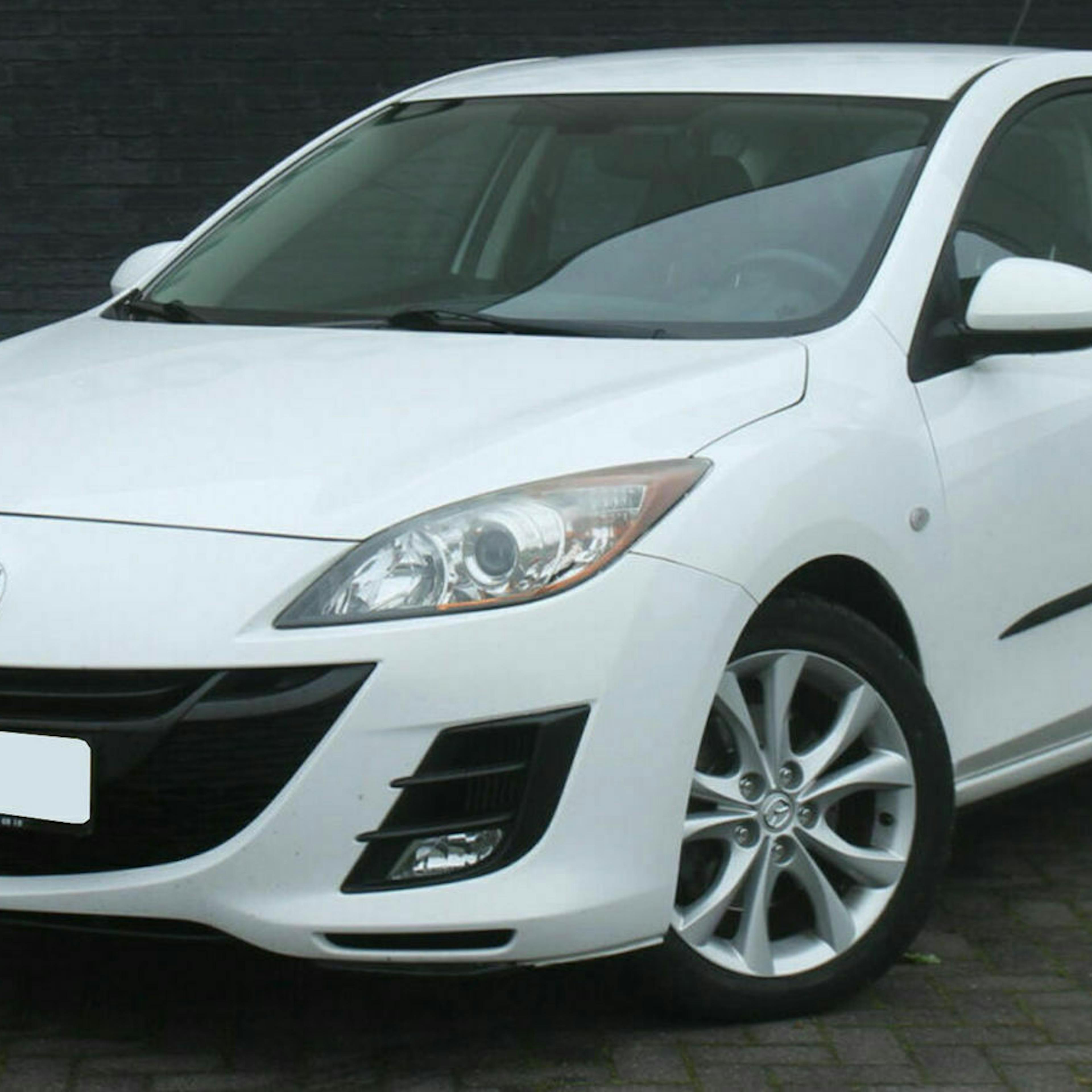 Ein weißer Mazda 3 BL steht vor einer grauen Wand