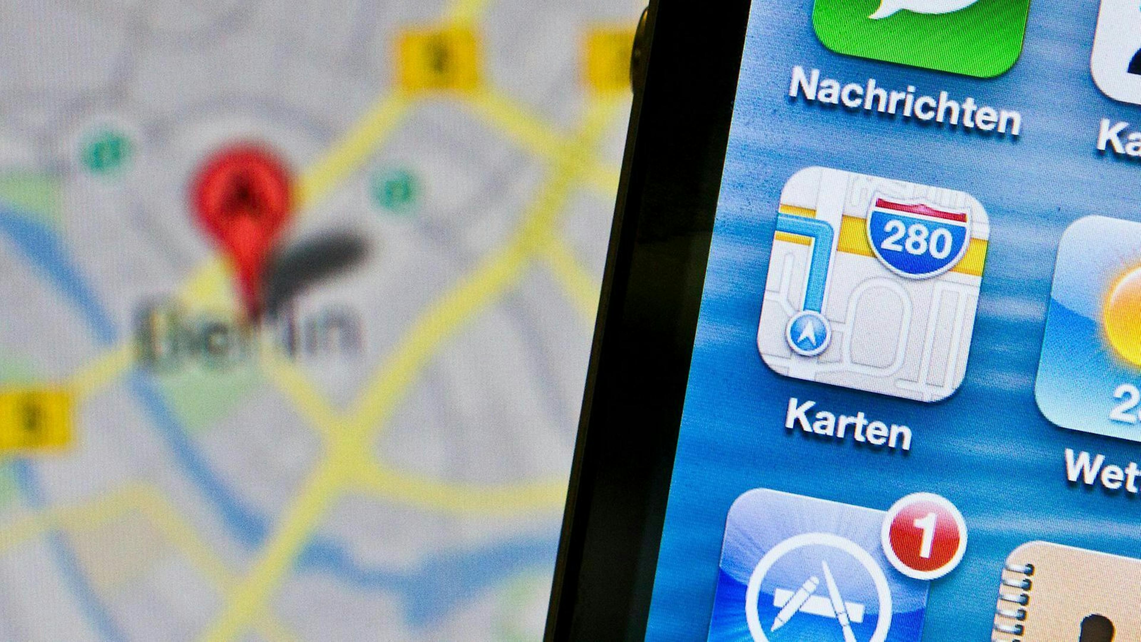 In Nahaufnahme ist das app-Symbol von Apples Kartendienst zu sehen während im Hintergrund eine Google Maps Karte geöffnet ist.