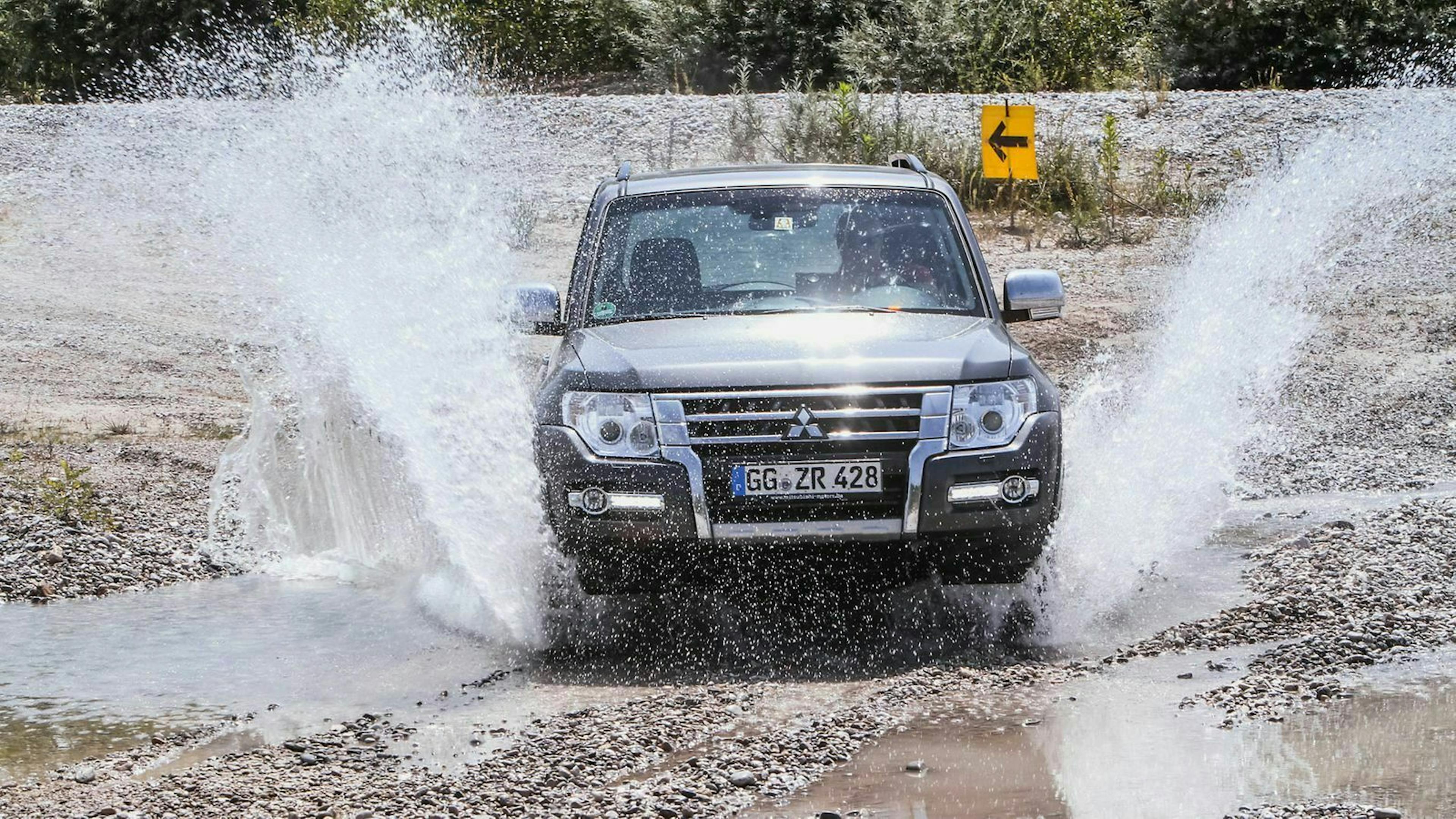 Ein Mitsubishi Pajero fährt durch einen Bachlauf in einem Schottergelände.