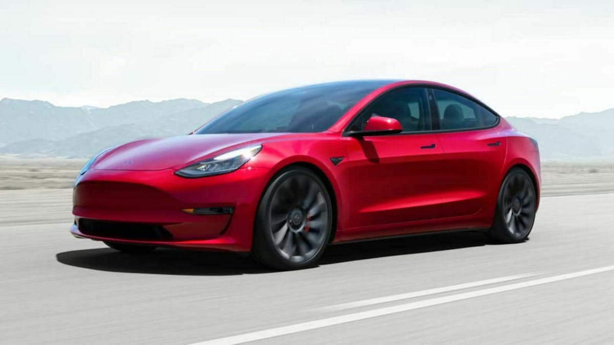 Ein roter Tesla Model 3 fährt eine Landstraße entlang