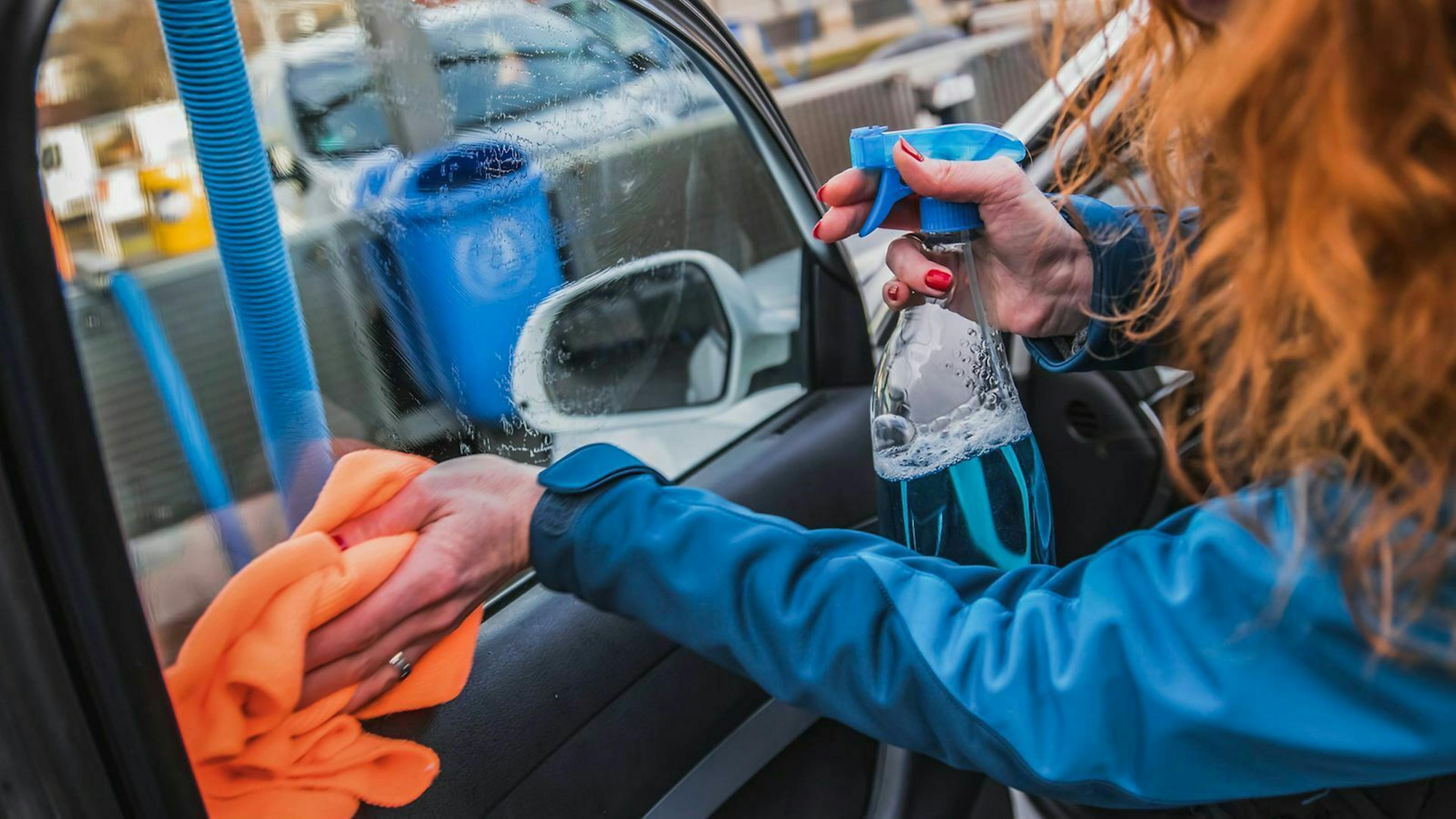 Eine Frau putzt die Seitenscheibe eines Autos.