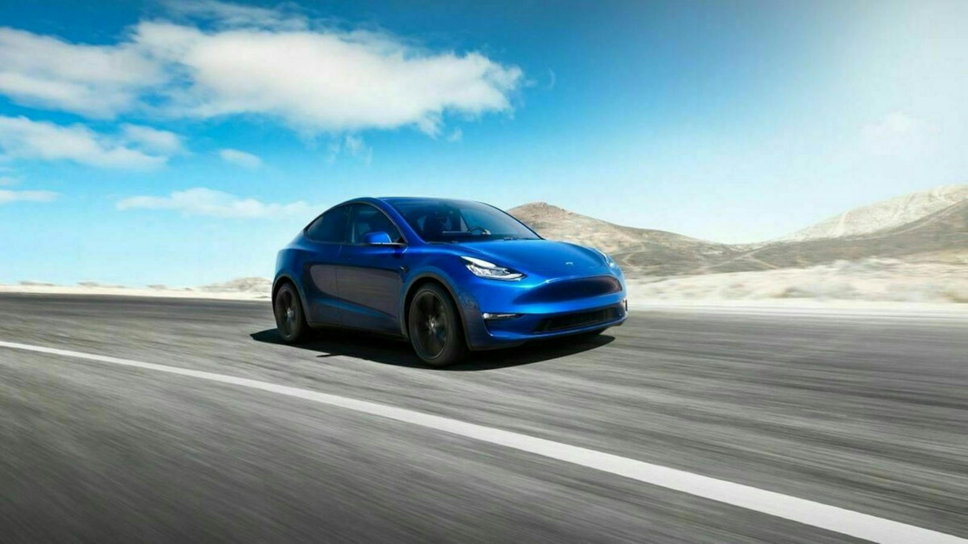 Ein blaues Tesla Model Y fährt eine Landstraße entlang