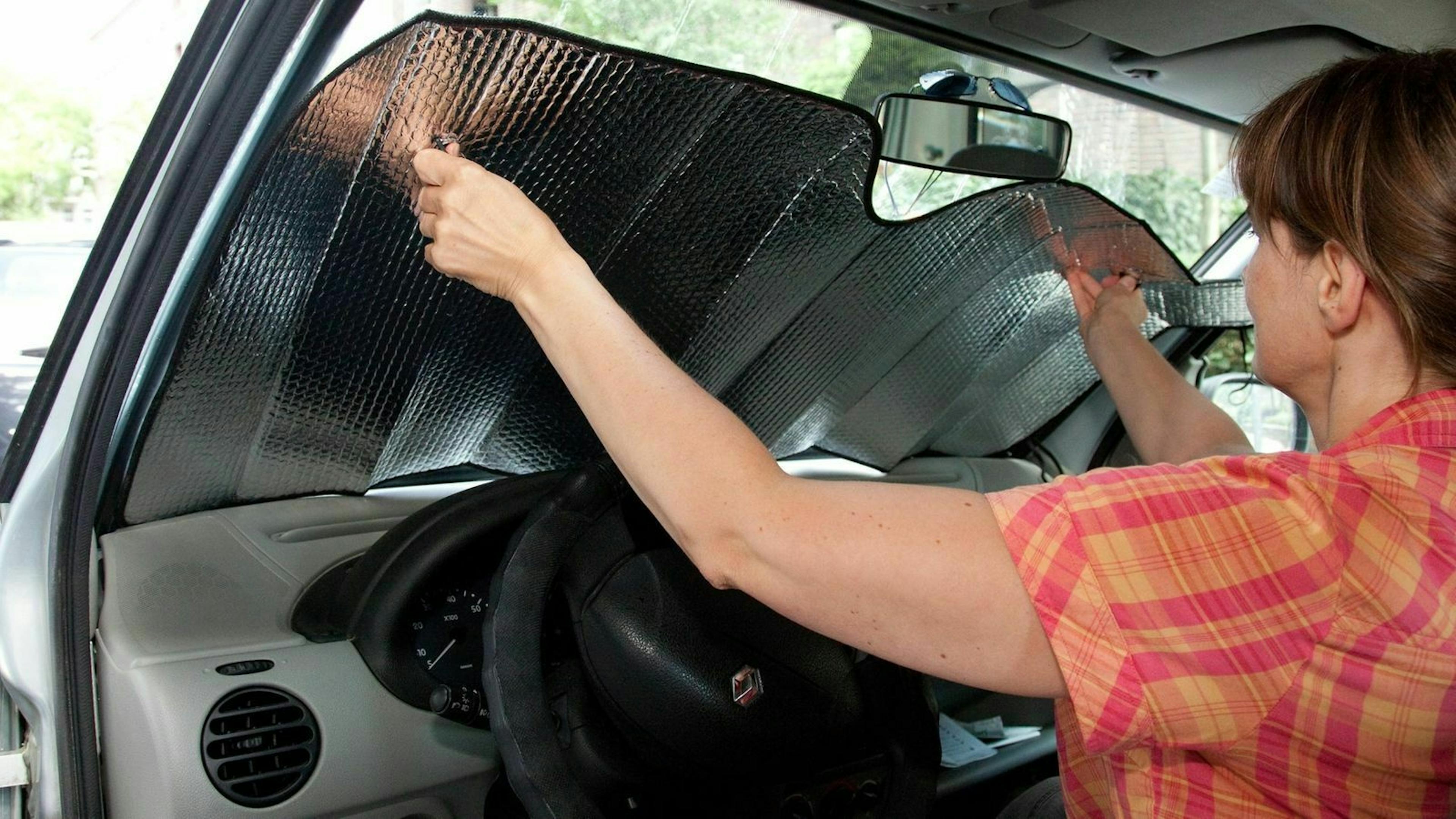 Zu sehen ist eine Frau, die eine Sonnenreflexionsfolie anbringt