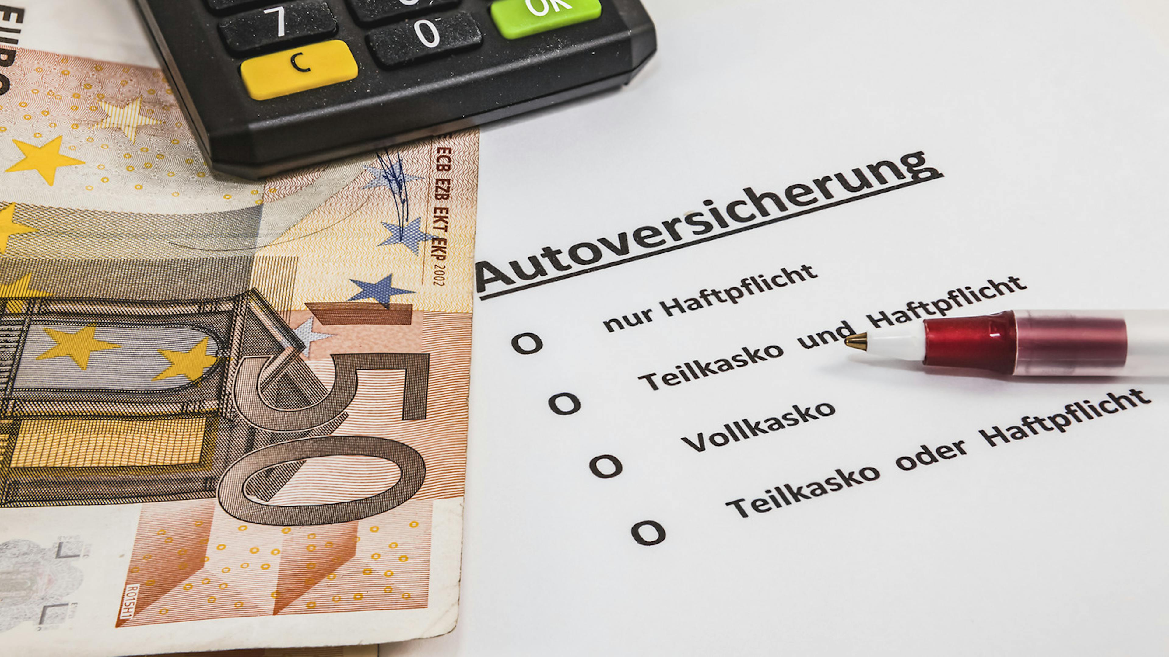 Ein Geldschein liegt auf einem Ausdruck einer Autoversicherung.