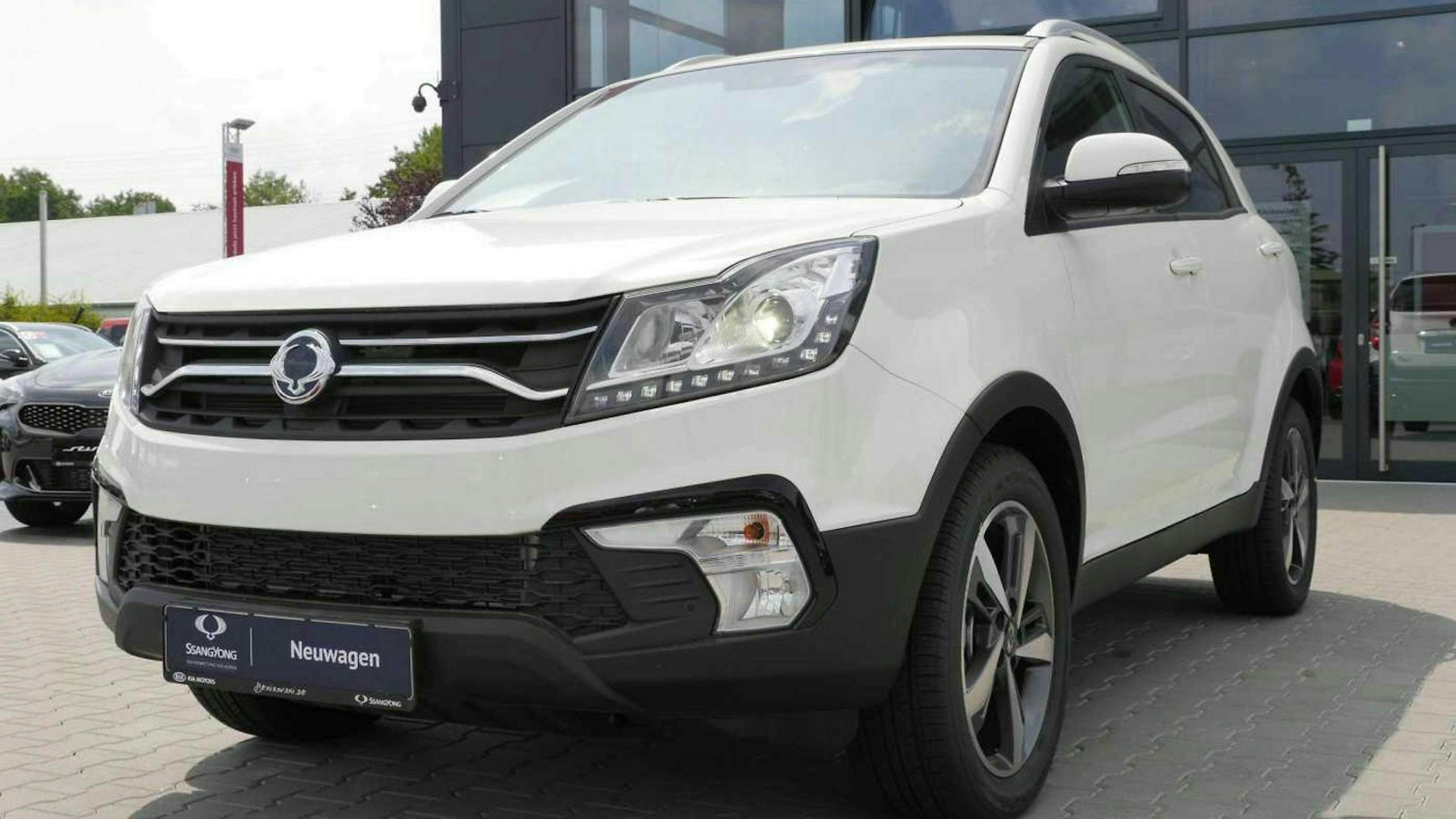 Ein weißer Neuwagen der Marke Ssangyong steht auf einem Stellplatz vor einem Autohaus.