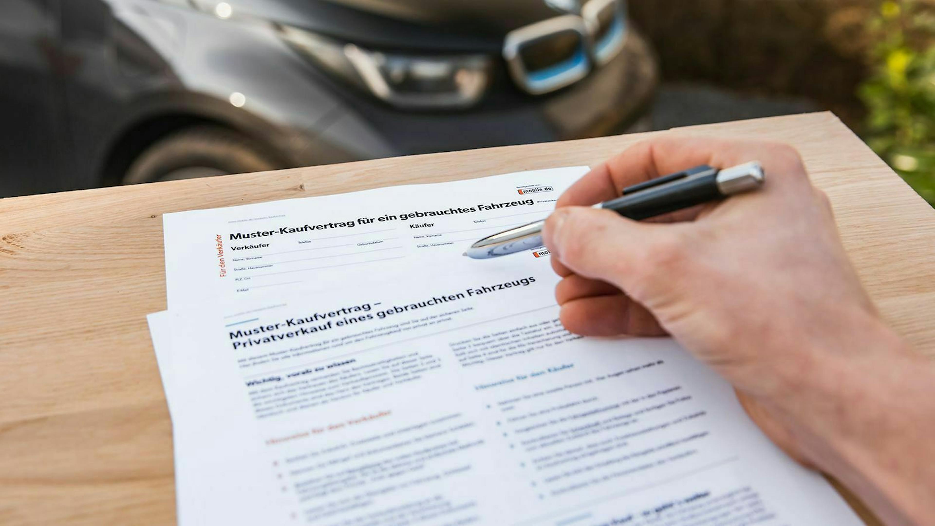 In der Ich-Perspektive füllt jemand mit einem Kugelschreiber den mobile.de-Kaufvertrag für Gebrauchtwagen aus.