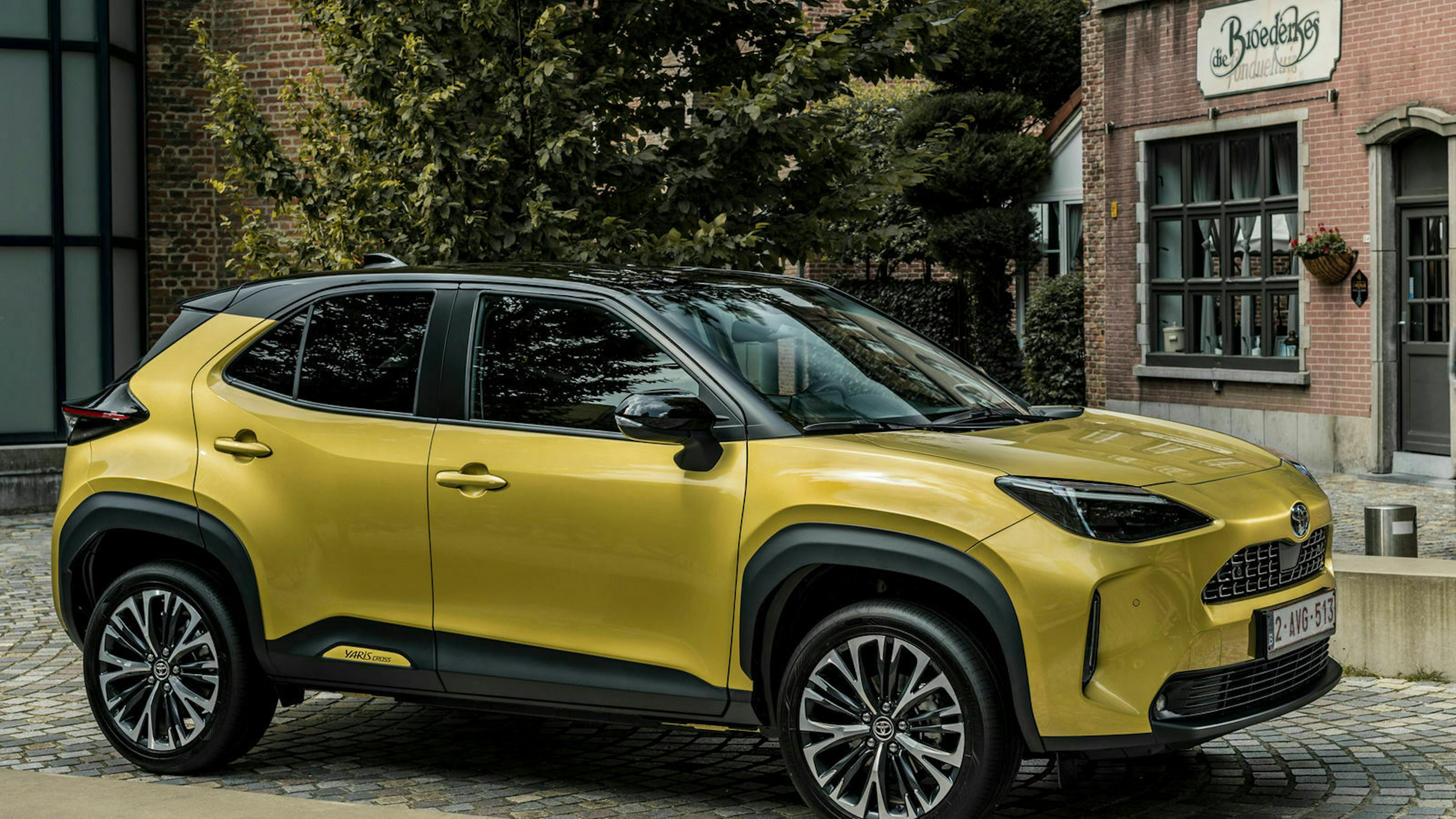 Ein gelber Toyota Yaris Cross steht vor einem braunen Gebäude